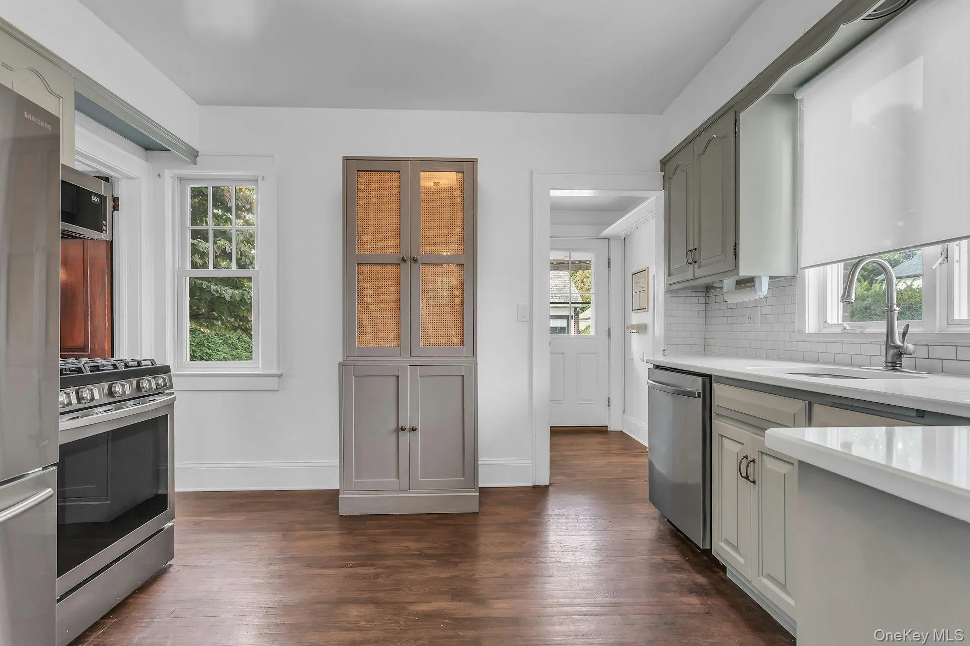 Stainless steel appliances, white subway tile backsplash, white countertops, built-in cabinetry, and wood-finish flooring Stainless steel appliances, white subway tile backsplash, white countertops, built-in cabinetry, and wood-finish flooring