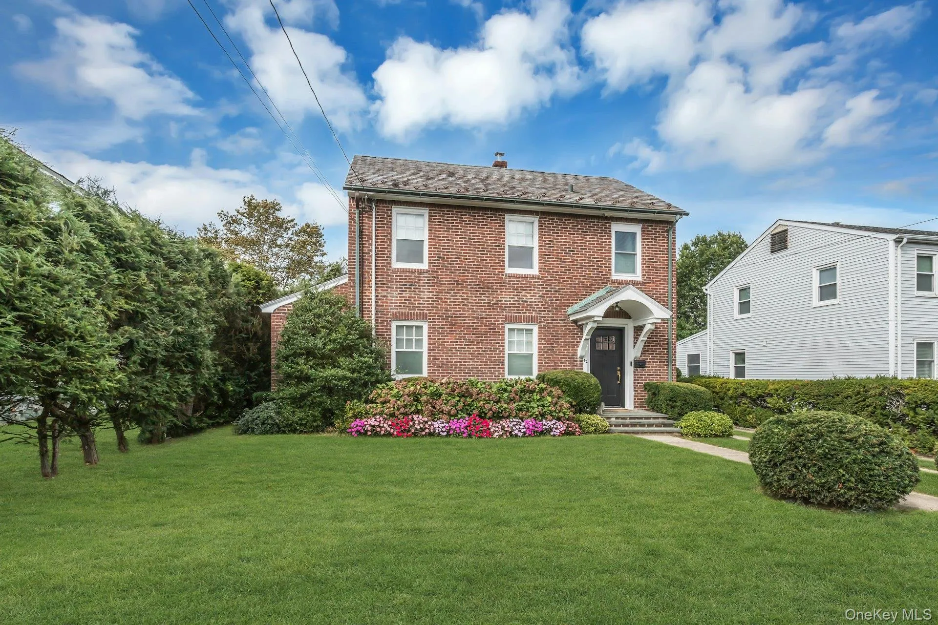 Brick exterior with a slate shingle roof, covered front entry, landscaped planting beds, and a concrete pathway Brick exterior with a slate shingle roof, covered front entry, landscaped planting beds, and a concrete pathway