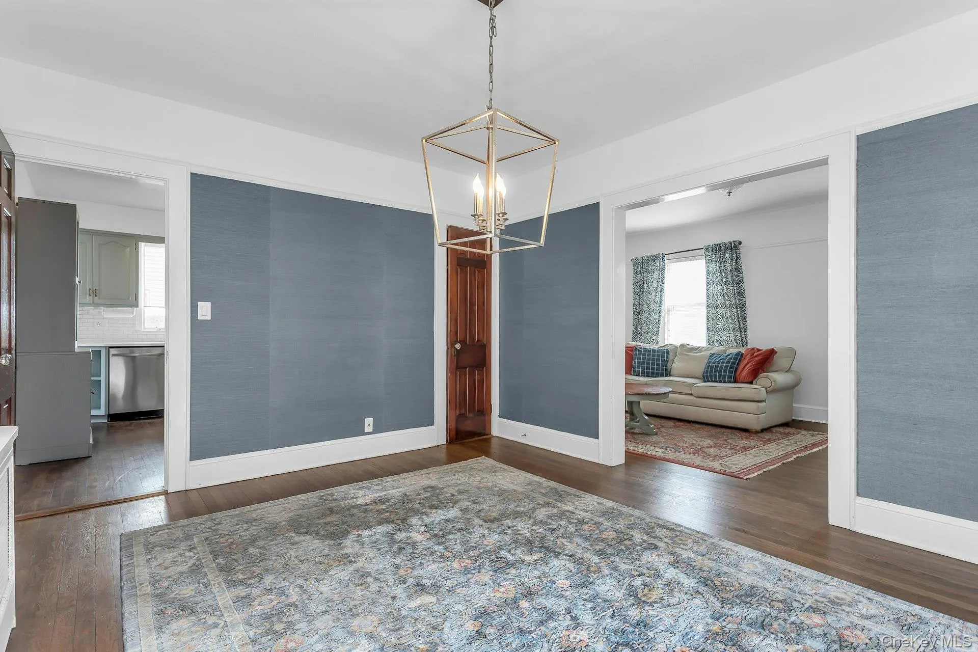 Hardwood flooring paired with a geometric metal chandelier, featuring an adjacent kitchen with stainless steel appliances and white subway tile backsplash, and a separate living space with a window Hardwood flooring paired with a geometric metal chandelier, featuring an adjacent kitchen with stainless steel appliances and white subway tile backsplash, and a separate living space with a window