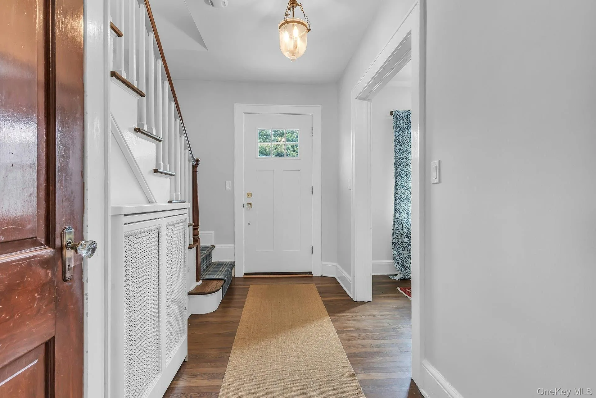Hardwood flooring, white paneled door with glass inserts, staircase with white risers and wood treads, built-in radiator cover, and hanging light fixture Hardwood flooring, white paneled door with glass inserts, staircase with white risers and wood treads, built-in radiator cover, and hanging light fixture