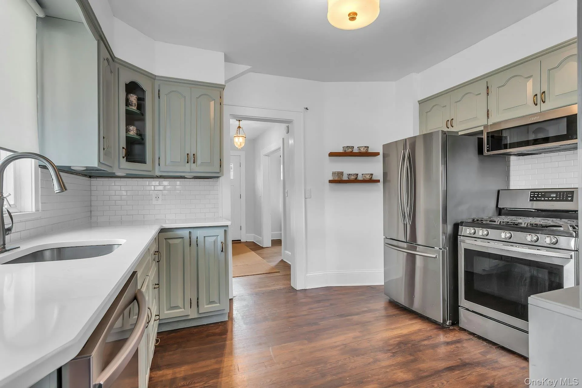 Kitchen featuring stainless steel appliances, wood-finish flooring, white countertops, subway tile backsplash, and light-toned cabinetry Kitchen featuring stainless steel appliances, wood-finish flooring, white countertops, subway tile backsplash, and light-toned cabinetry