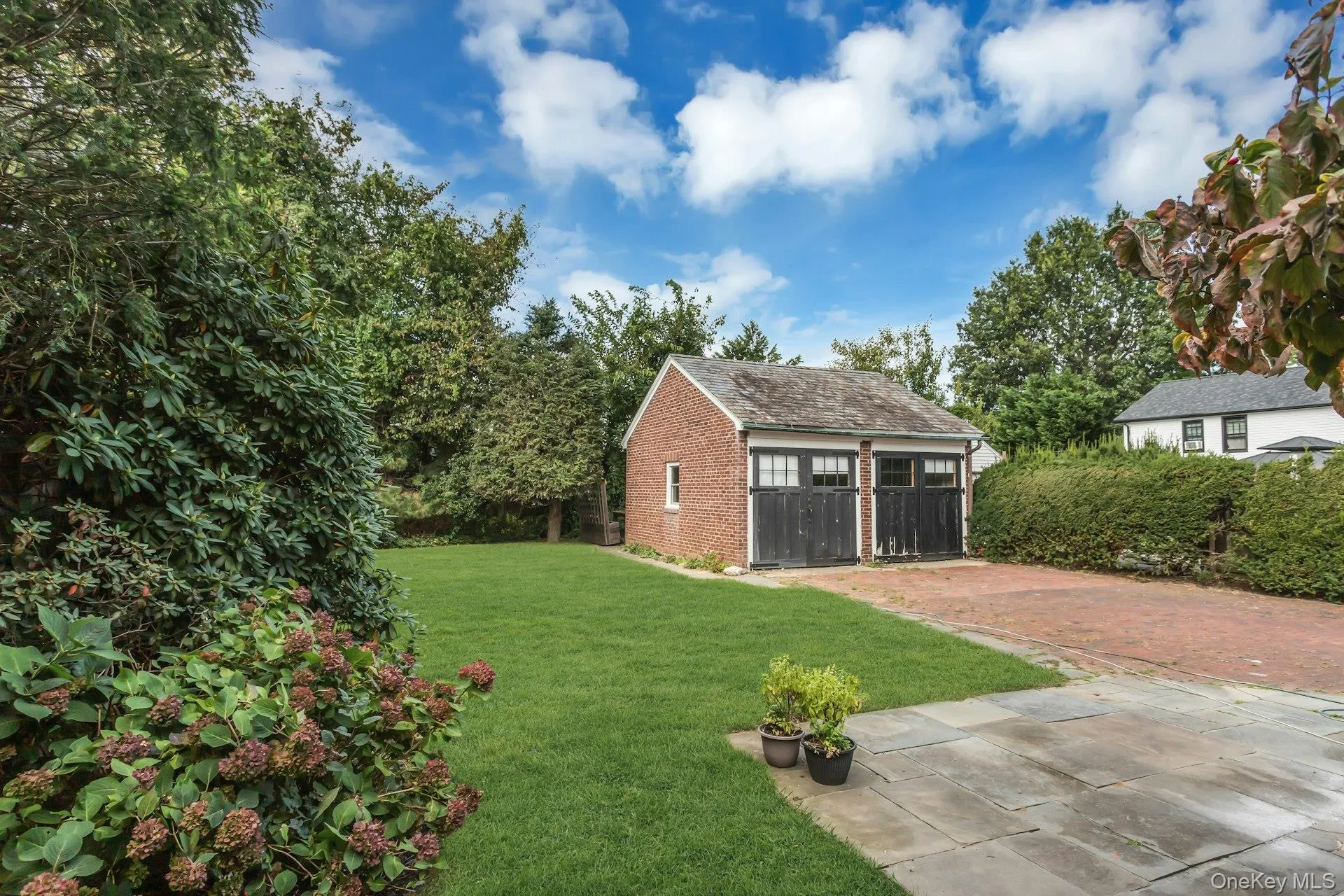 Brick garage with two carriage-style doors, a natural stone patio, and a brick paver driveway Brick garage with two carriage-style doors, a natural stone patio, and a brick paver driveway