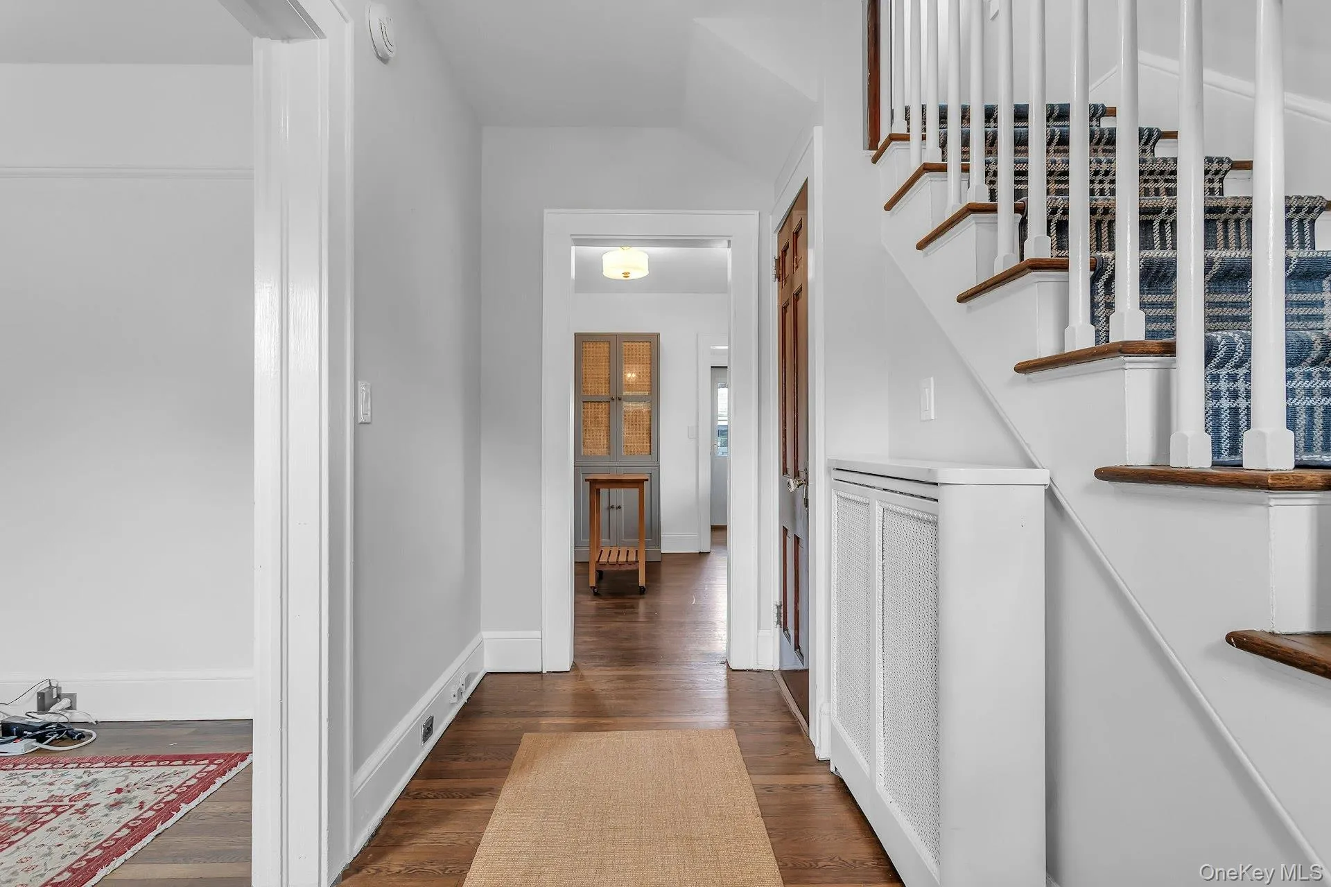Hardwood flooring, painted white baseboards, a staircase with white balusters and wood-finish treads, and a built-in radiator cover Hardwood flooring, painted white baseboards, a staircase with white balusters and wood-finish treads, and a built-in radiator cover