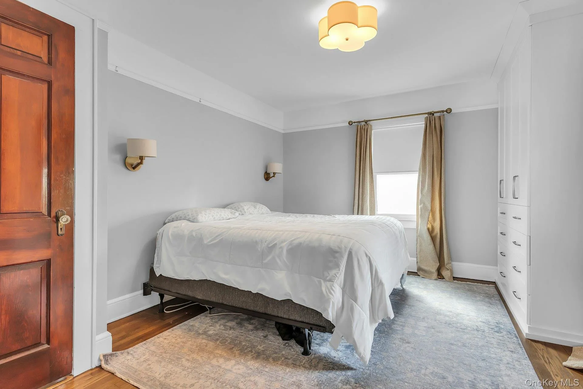 Hardwood flooring, crown molding, built-in cabinetry, two wall sconces, and a ceiling-mounted light fixture Hardwood flooring, crown molding, built-in cabinetry, two wall sconces, and a ceiling-mounted light fixture