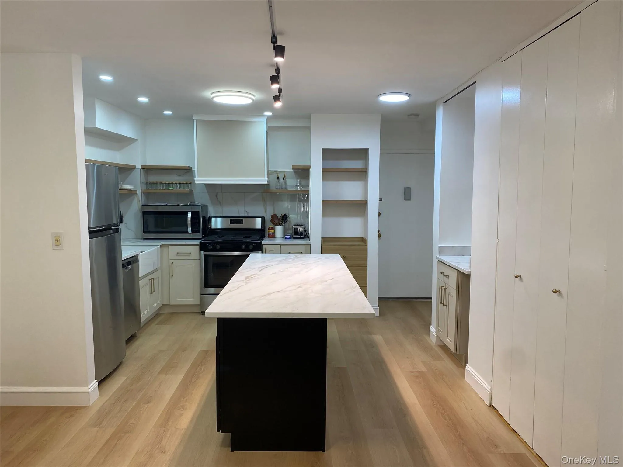 Kitchen featuring wood-finish flooring, stainless steel appliances, a center island with a white countertop, recessed lighting, and white cabinetry Kitchen featuring wood-finish flooring, stainless steel appliances, a center island with a white countertop, recessed lighting, and white cabinetry