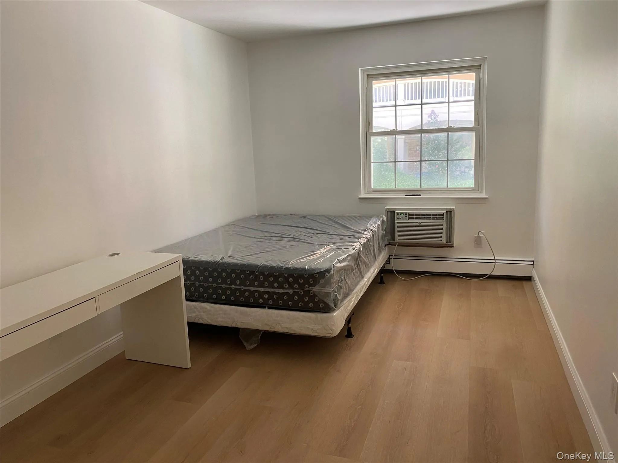 Light-filled room featuring wood-finish flooring, a window with grid panes, and a wall-mounted air conditioning unit Light-filled room featuring wood-finish flooring, a window with grid panes, and a wall-mounted air conditioning unit