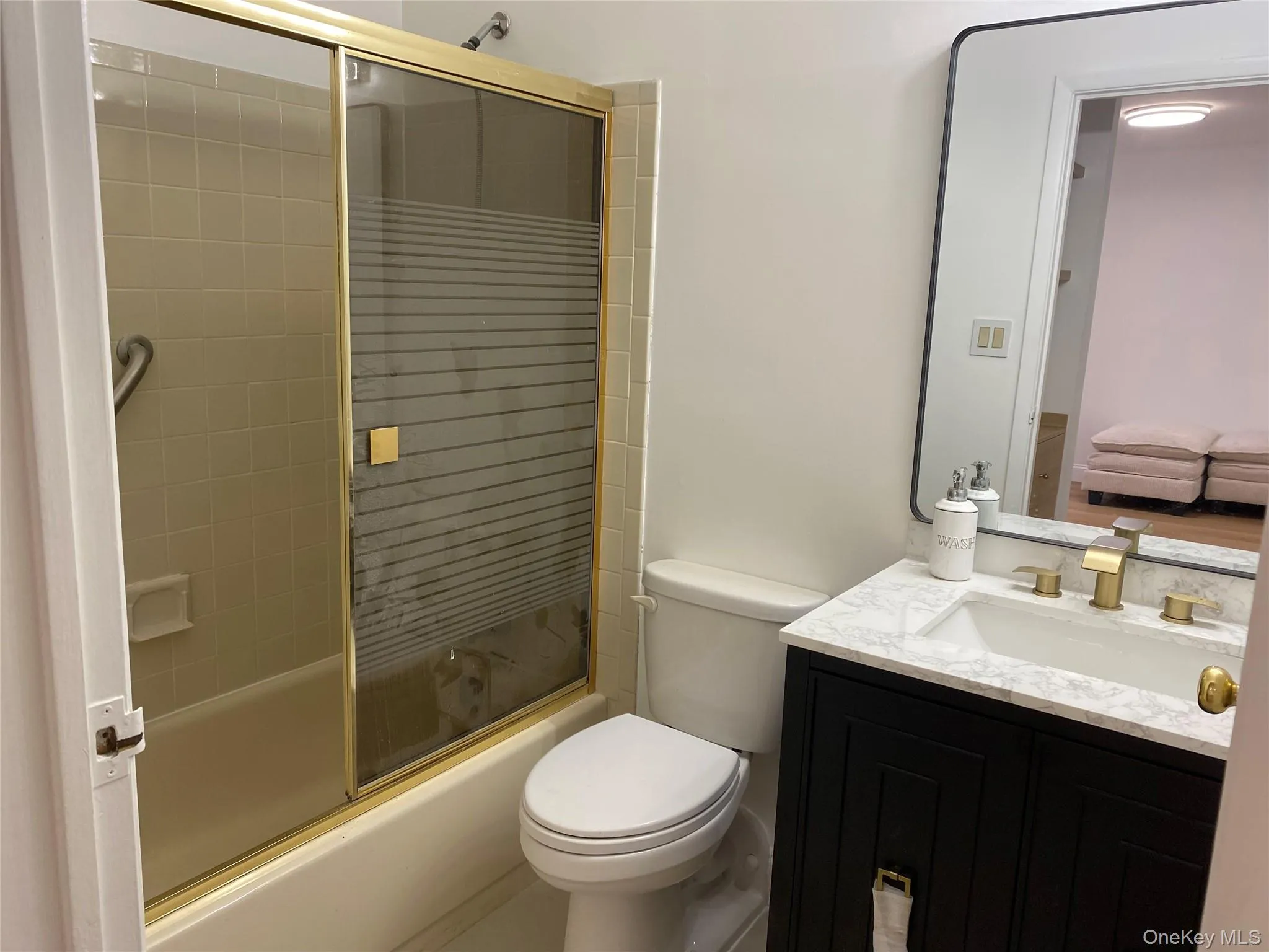 Tub/shower combination with gold-toned sliding glass door, white tile wall surround, and grab bar Tub/shower combination with gold-toned sliding glass door, white tile wall surround, and grab bar