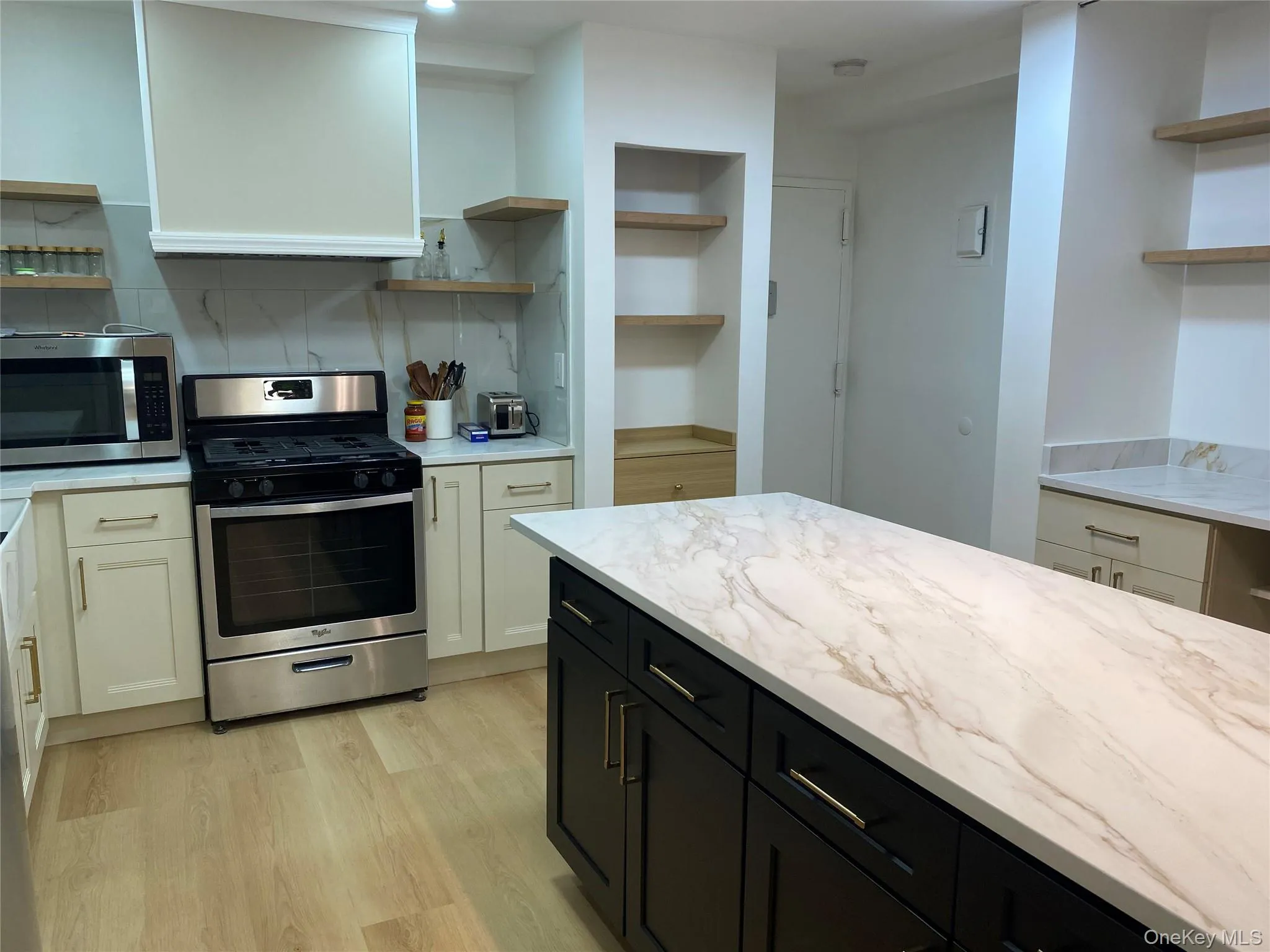 Kitchen featuring a central island with a light-toned countertop, stainless steel range, white cabinetry, and wood-finish flooring Kitchen featuring a central island with a light-toned countertop, stainless steel range, white cabinetry, and wood-finish flooring