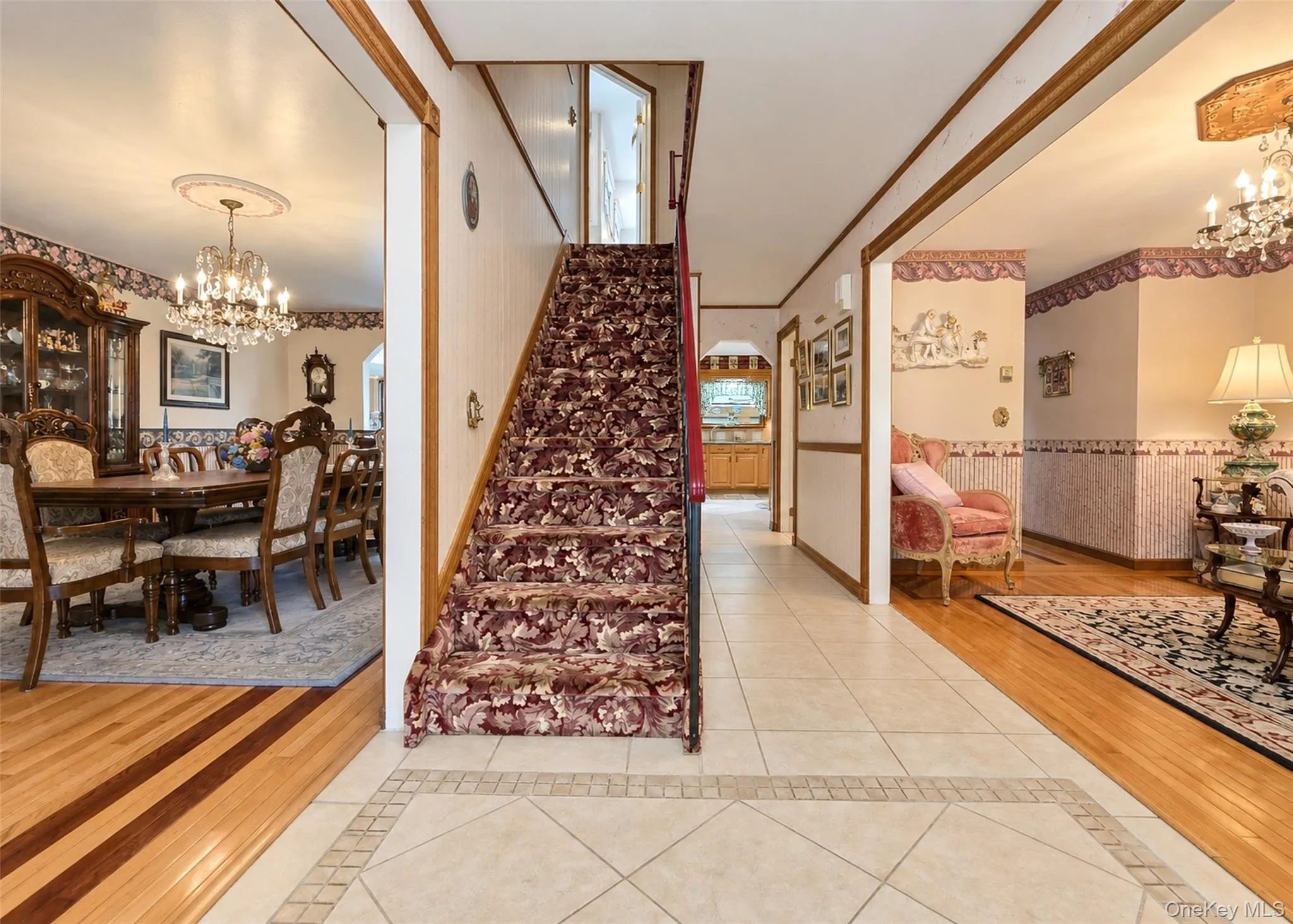 Hardwood flooring with inlay accents, ceramic tile flooring, staircase with patterned carpeting, recessed archway, and an ornate chandelier Hardwood flooring with inlay accents, ceramic tile flooring, staircase with patterned carpeting, recessed archway, and an ornate chandelier