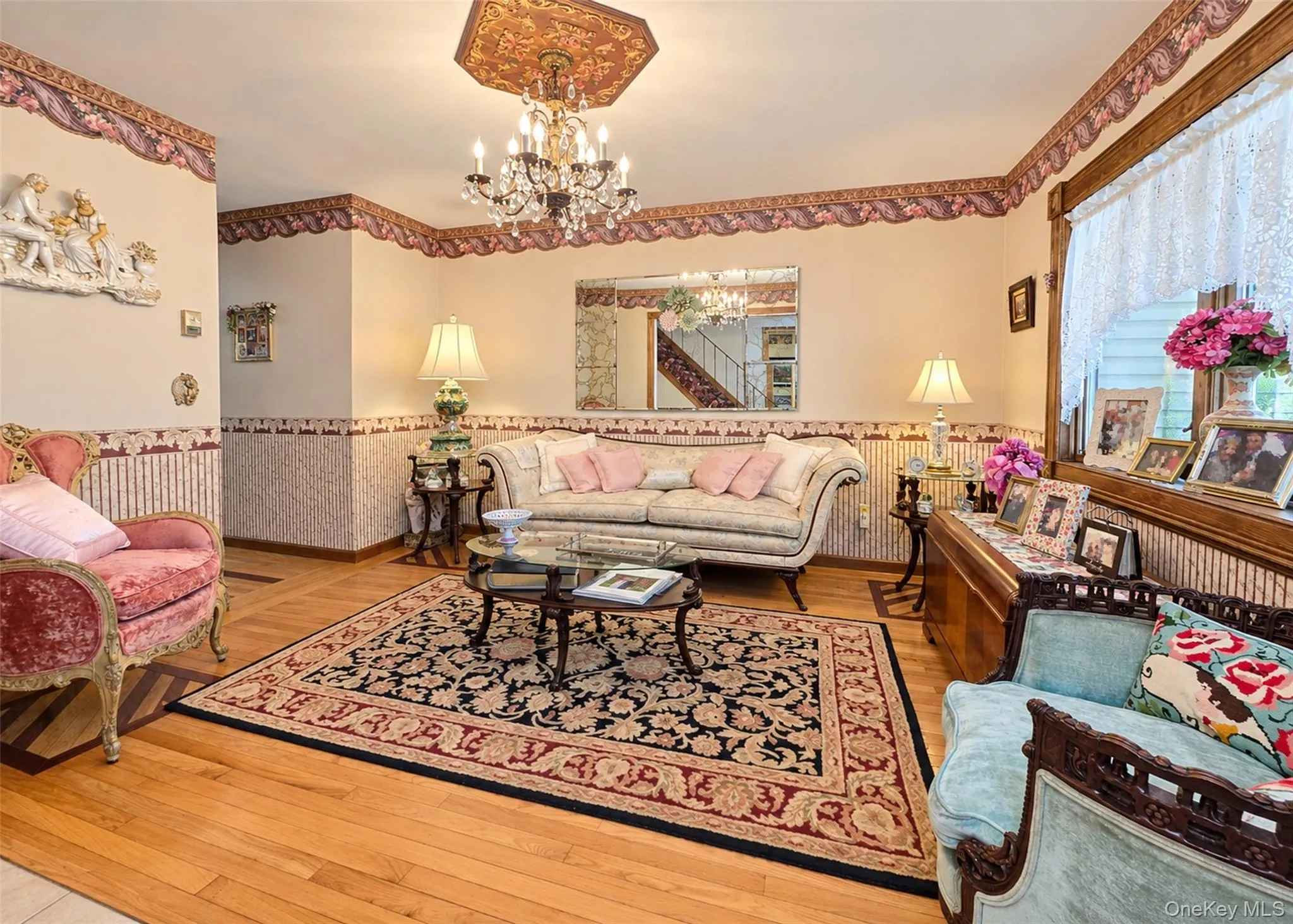 Hardwood flooring with decorative inlay, chandelier with ornate ceiling medallion, decorative wall coverings, window with lace curtain, and built-in wood trim Hardwood flooring with decorative inlay, chandelier with ornate ceiling medallion, decorative wall coverings, window with lace curtain, and built-in wood trim