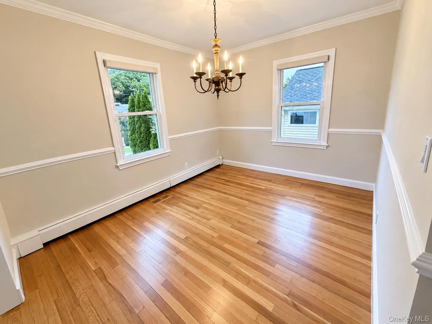 Hardwood flooring, crown molding, chair rail molding, two windows, and a chandelier with a wood-tone accent Hardwood flooring, crown molding, chair rail molding, two windows, and a chandelier with a wood-tone accent