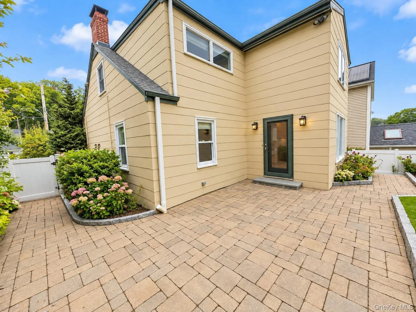 Expansive paver patio with a rear entry door, exterior lighting, and landscaped garden beds Expansive paver patio with a rear entry door, exterior lighting, and landscaped garden beds