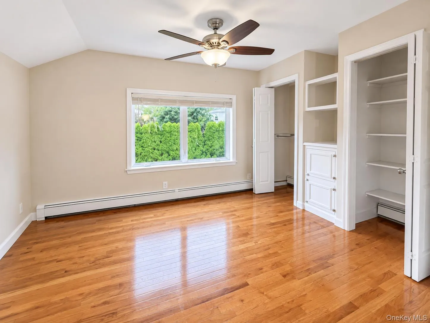 Vaulted ceiling with a ceiling fan, hardwood flooring, built-in shelving, built-in cabinetry, and a window overlooking greenery Vaulted ceiling with a ceiling fan, hardwood flooring, built-in shelving, built-in cabinetry, and a window overlooking greenery
