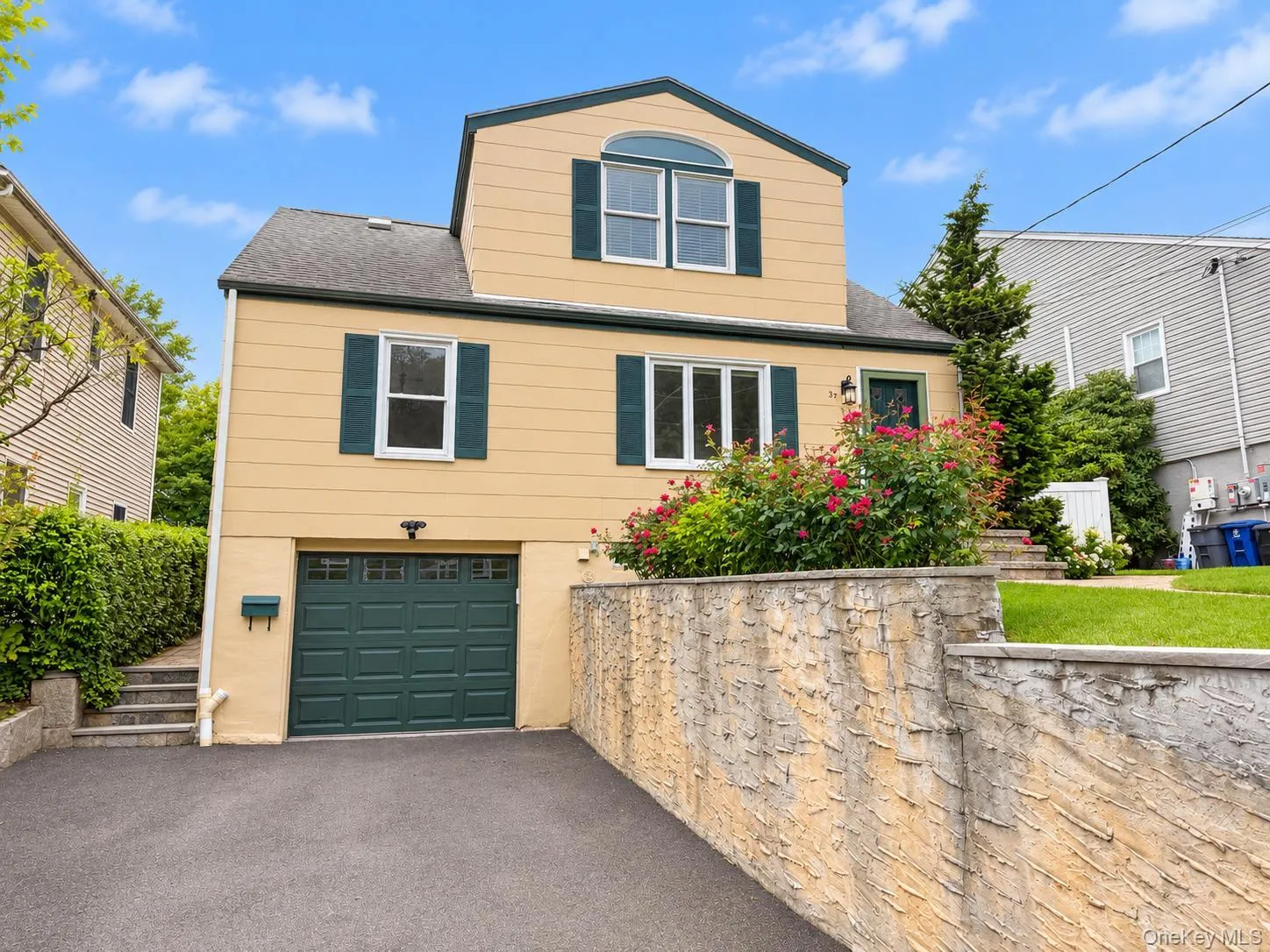 Yellow exterior with dark green shutters, a peaked dormer, and a ground-level garage Yellow exterior with dark green shutters, a peaked dormer, and a ground-level garage