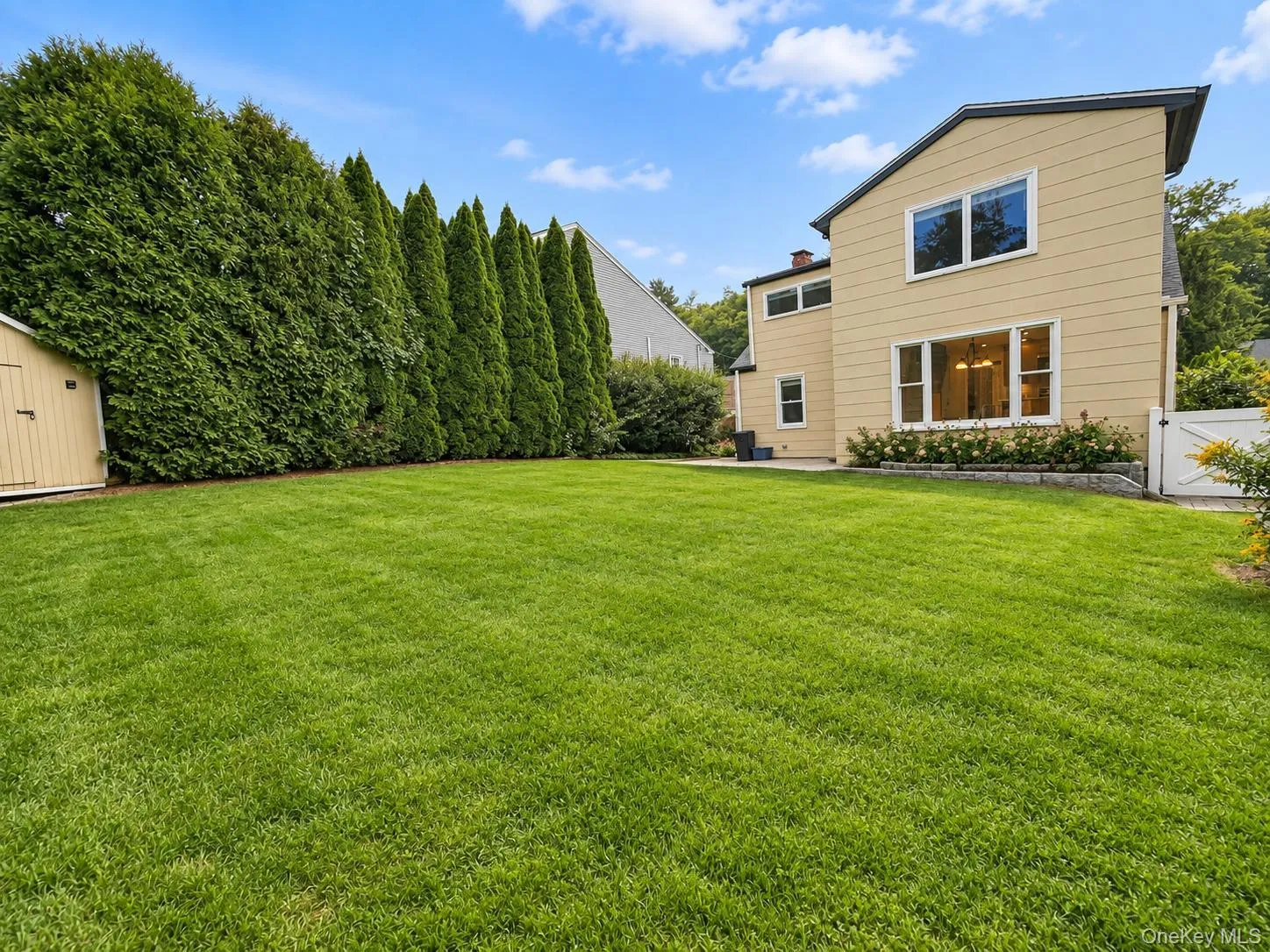 Expansive green lawn, mature perimeter landscaping, light-colored siding, and white window trim Expansive green lawn, mature perimeter landscaping, light-colored siding, and white window trim