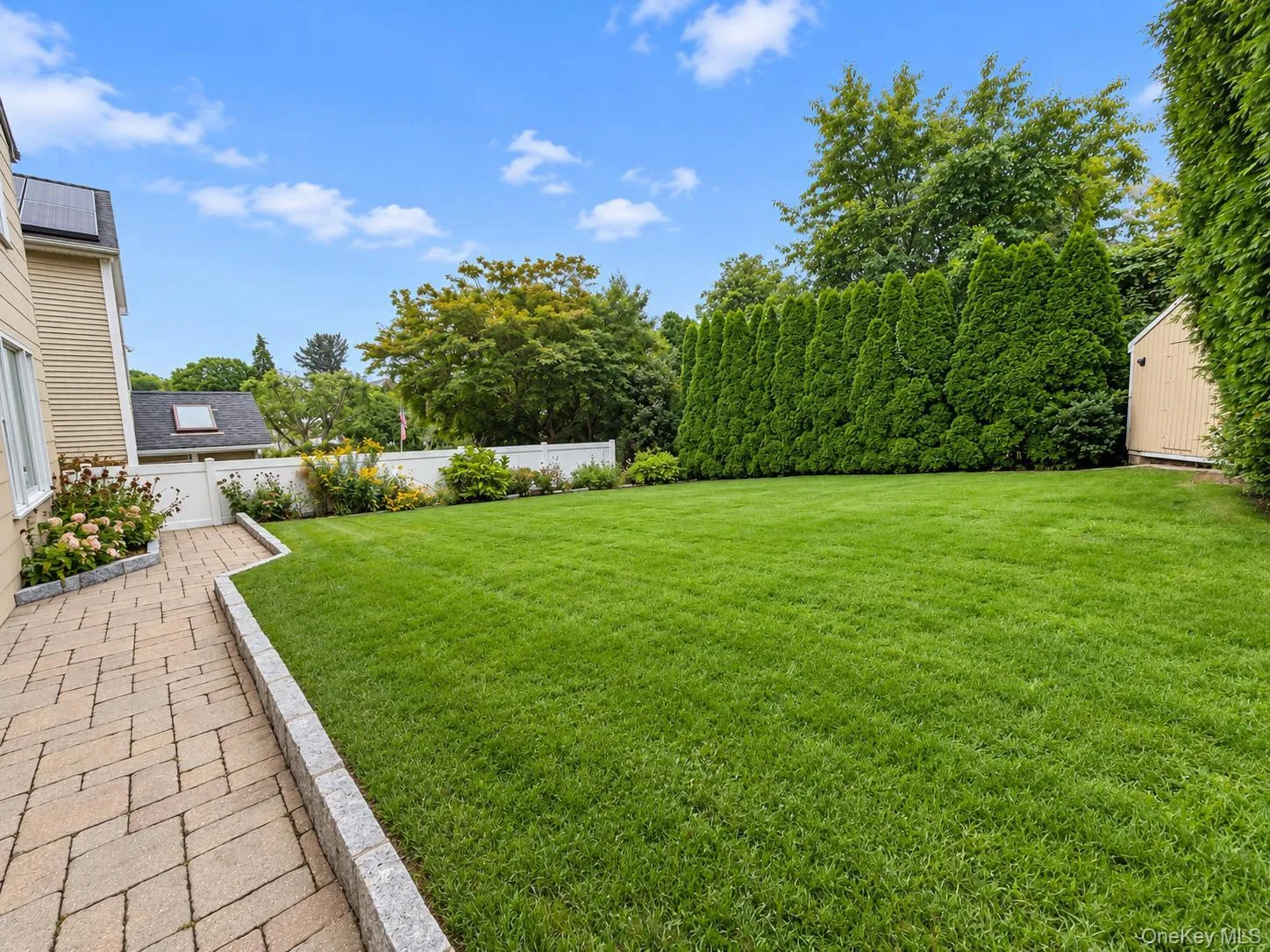 Expansive green lawn, paver patio, stone retaining wall, established privacy hedging, and garden shed Expansive green lawn, paver patio, stone retaining wall, established privacy hedging, and garden shed