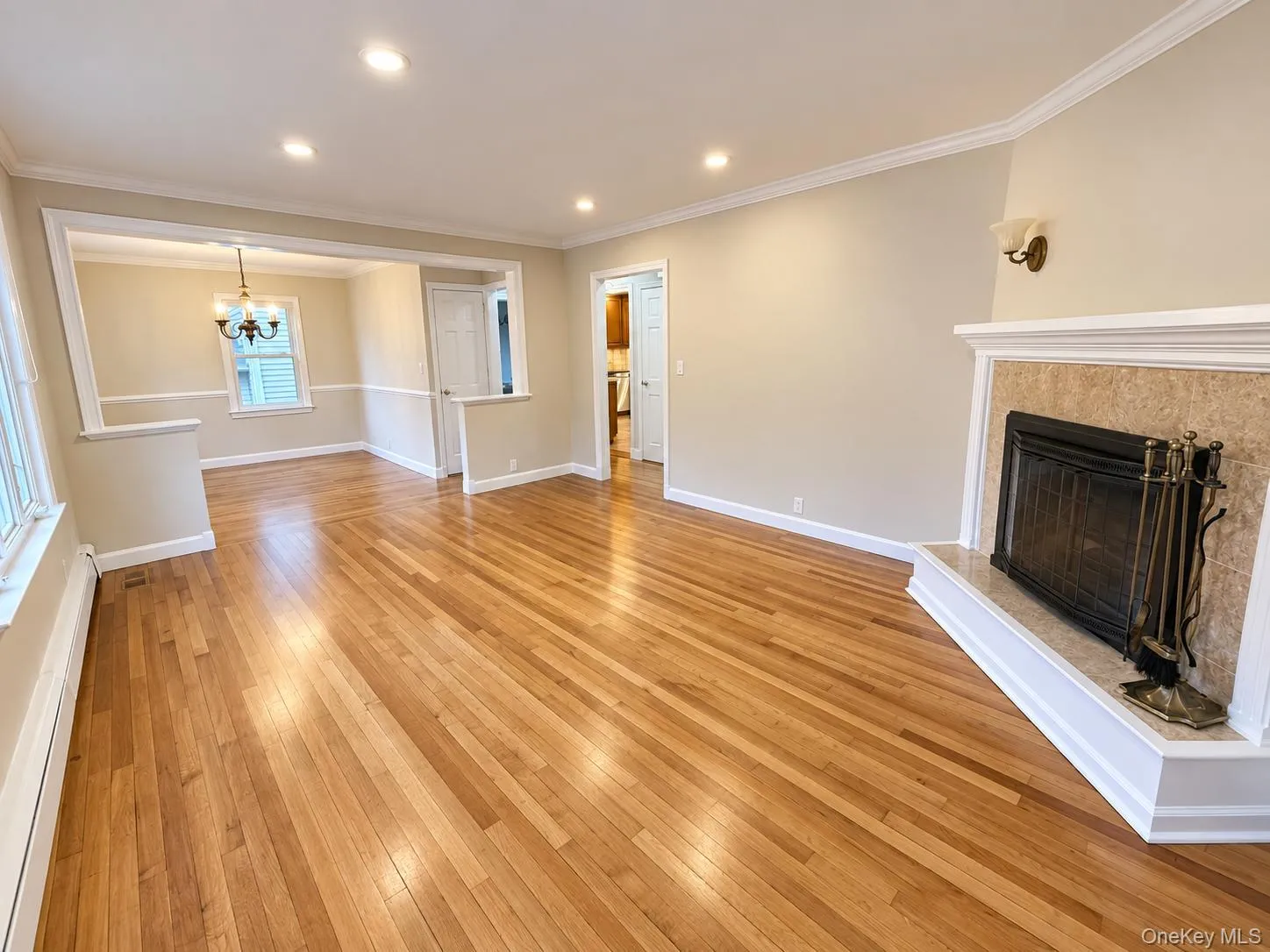 Hardwood flooring throughout, recessed lighting, crown molding, fireplace with stone surround, and an open entryway to an additional room with a chandelier Hardwood flooring throughout, recessed lighting, crown molding, fireplace with stone surround, and an open entryway to an additional room with a chandelier