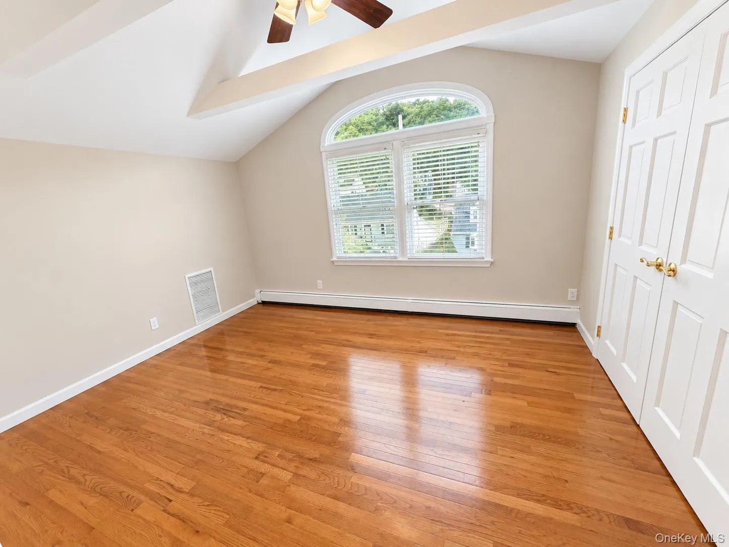 Vaulted ceiling with exposed beams, ceiling fan, hardwood flooring, arched window, and paneled bifold closet doors Vaulted ceiling with exposed beams, ceiling fan, hardwood flooring, arched window, and paneled bifold closet doors