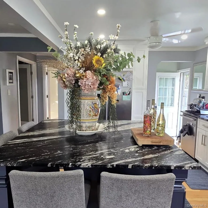 Kitchen island with a dark granite countertop, recessed lighting, white cabinetry, a ceiling fan, and stainless steel appliances Kitchen island with a dark granite countertop, recessed lighting, white cabinetry, a ceiling fan, and stainless steel appliances