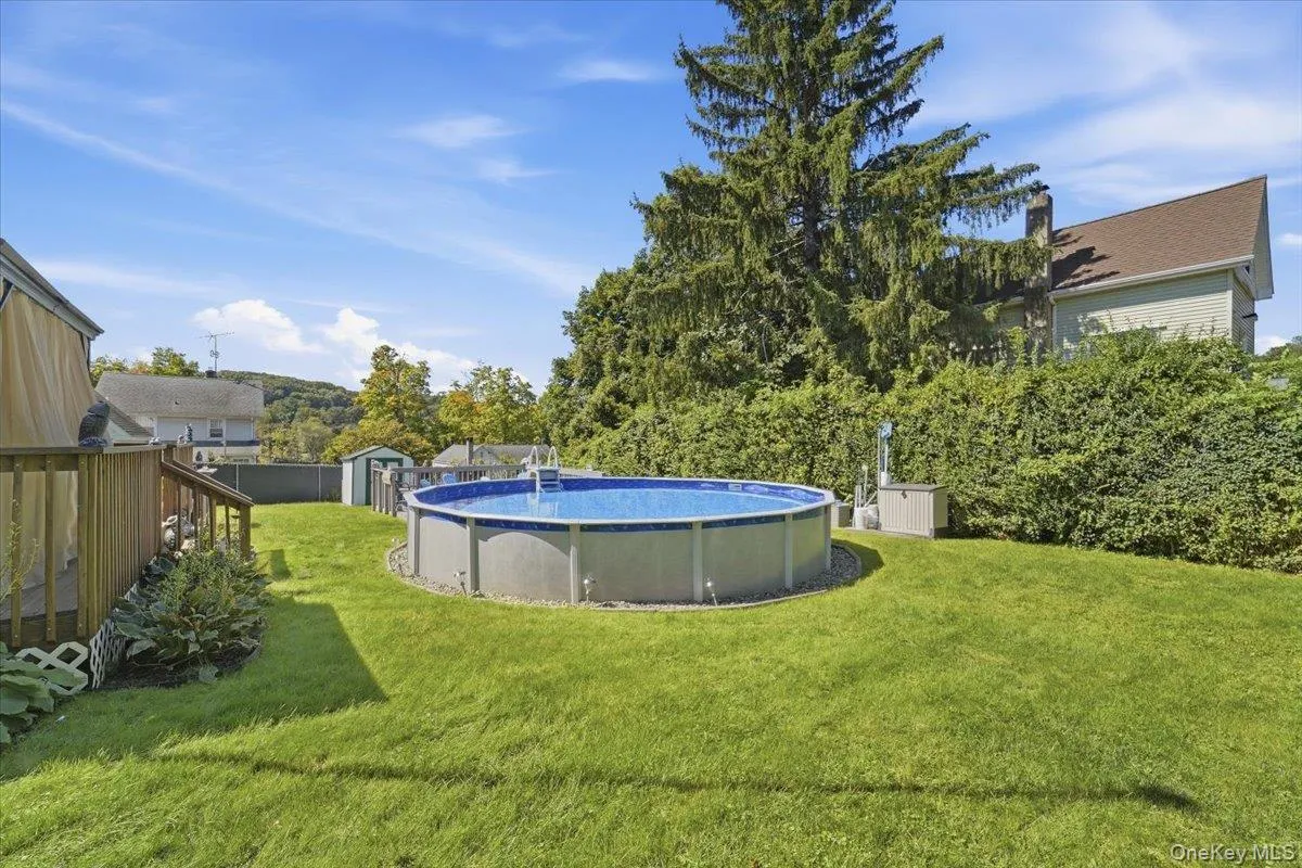 Expansive backyard featuring a manicured lawn, a round above-ground pool, and a wooden deck with railings Expansive backyard featuring a manicured lawn, a round above-ground pool, and a wooden deck with railings