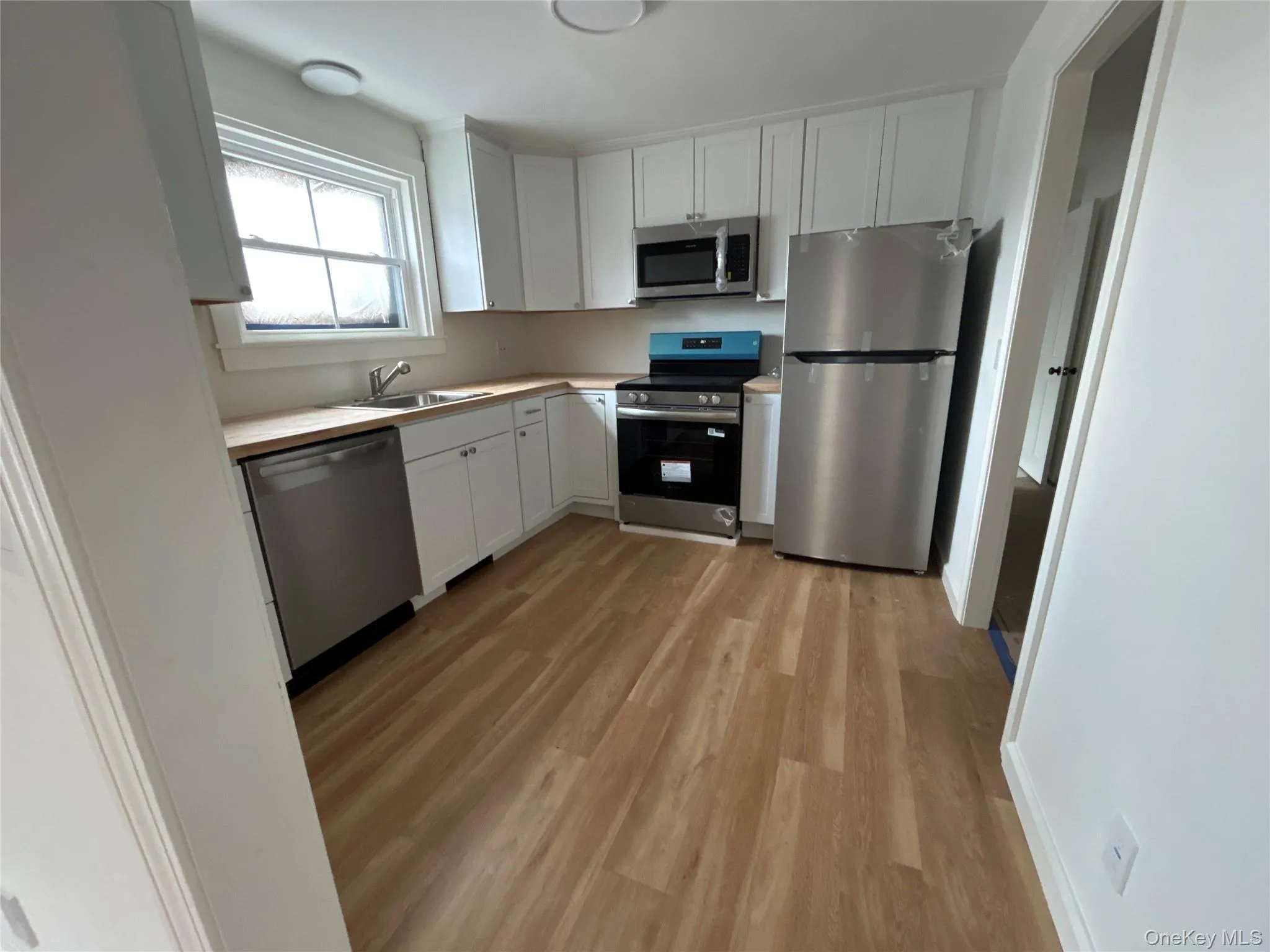 Kitchen featuring stainless steel appliances, light countertops, white cabinetry, and laminate floors Kitchen featuring stainless steel appliances, light countertops, white cabinetry, and laminate floors