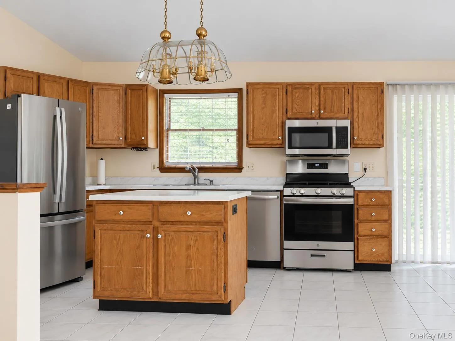 Kitchen featuring wood cabinetry, stainless steel appliances, a center island, and tiled flooring Kitchen featuring wood cabinetry, stainless steel appliances, a center island, and tiled flooring