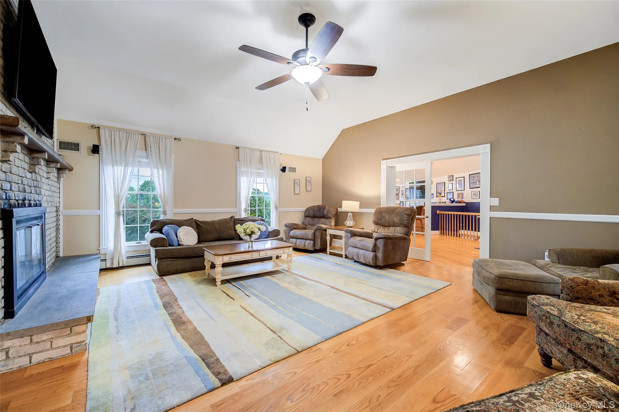 Vaulted ceiling, ceiling fan, wood-finish flooring, brick fireplace with stone hearth, and double glass-paneled doors to Bonus room Vaulted ceiling, ceiling fan, wood-finish flooring, brick fireplace with stone hearth, and double glass-paneled doors to Bonus room