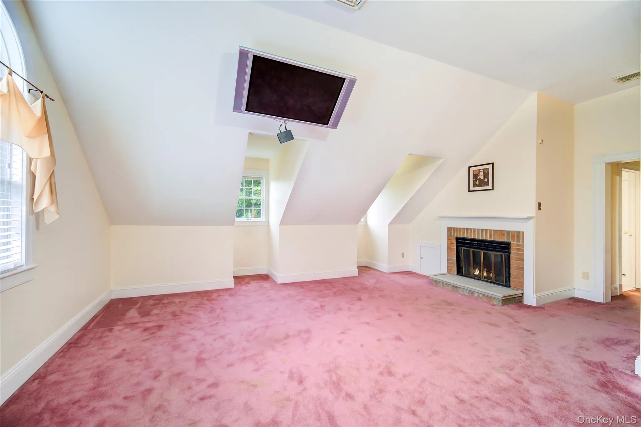 Sloped ceiling room featuring a brick fireplace with stone hearth, multiple windows for sun/moonlight Sloped ceiling room featuring a brick fireplace with stone hearth, multiple windows for sun/moonlight