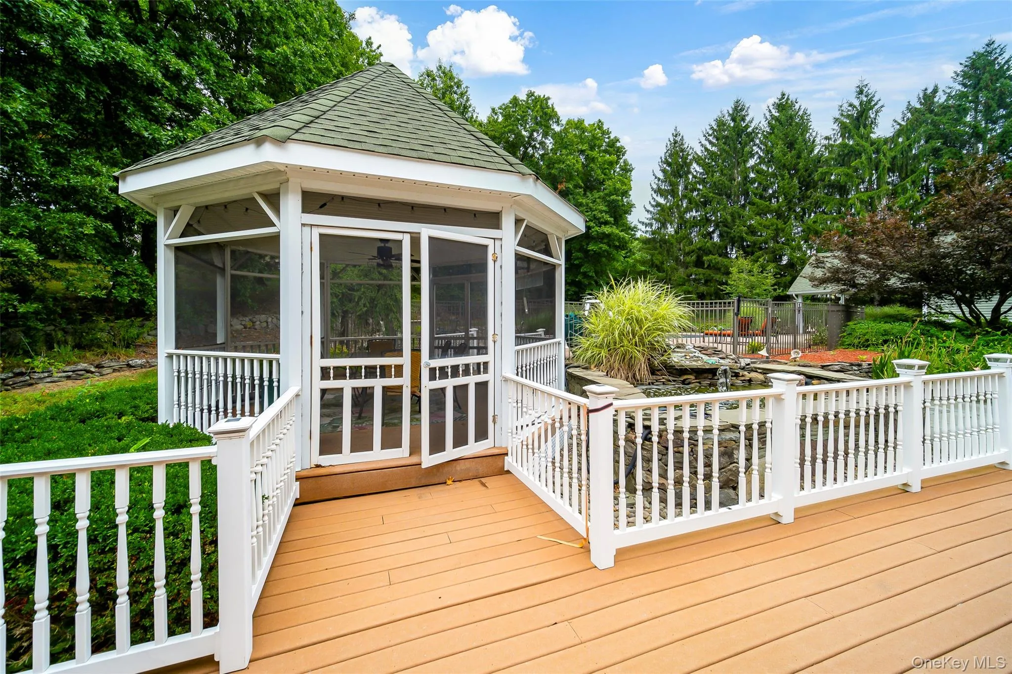 Screened gazebo with a multi-level deck, white baluster railings, and a built-in water feature Screened gazebo with a multi-level deck, white baluster railings, and a built-in water feature