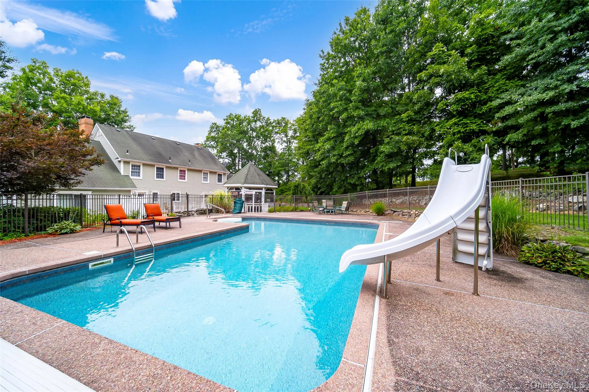 In-ground swimming pool with a slide, surrounded by a concrete pool deck, and a detached gazebo In-ground swimming pool with a slide, surrounded by a concrete pool deck, and a detached gazebo