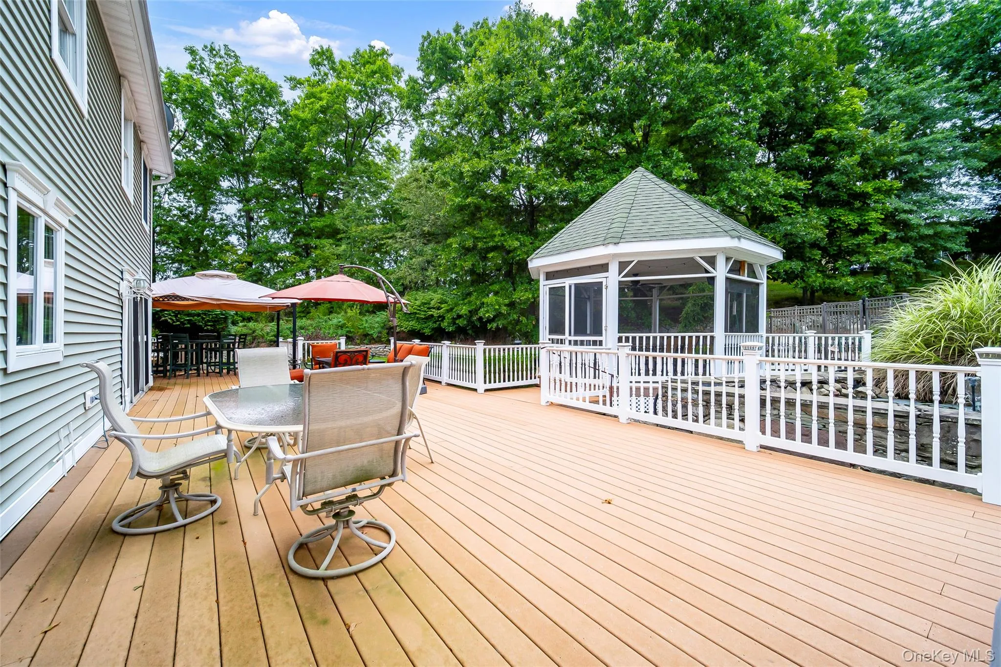 Expansive outdoor deck featuring a screened gazebo, white railing system, and adjacent green space Expansive outdoor deck featuring a screened gazebo, white railing system, and adjacent green space