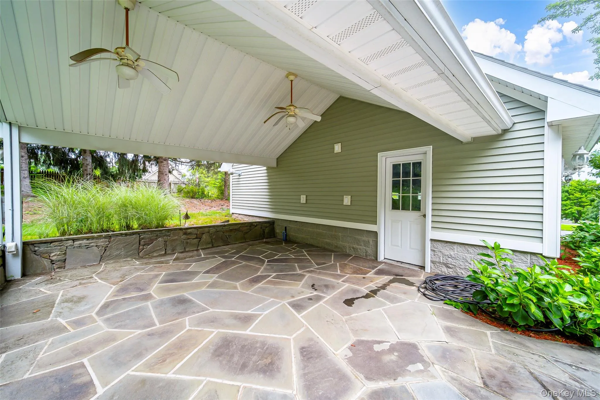 Covered outdoor patio featuring a flagstone surface, stone retaining wall, and two ceiling fans. Perfect for outdoor kitchen! Covered outdoor patio featuring a flagstone surface, stone retaining wall, and two ceiling fans. Perfect for outdoor kitchen!