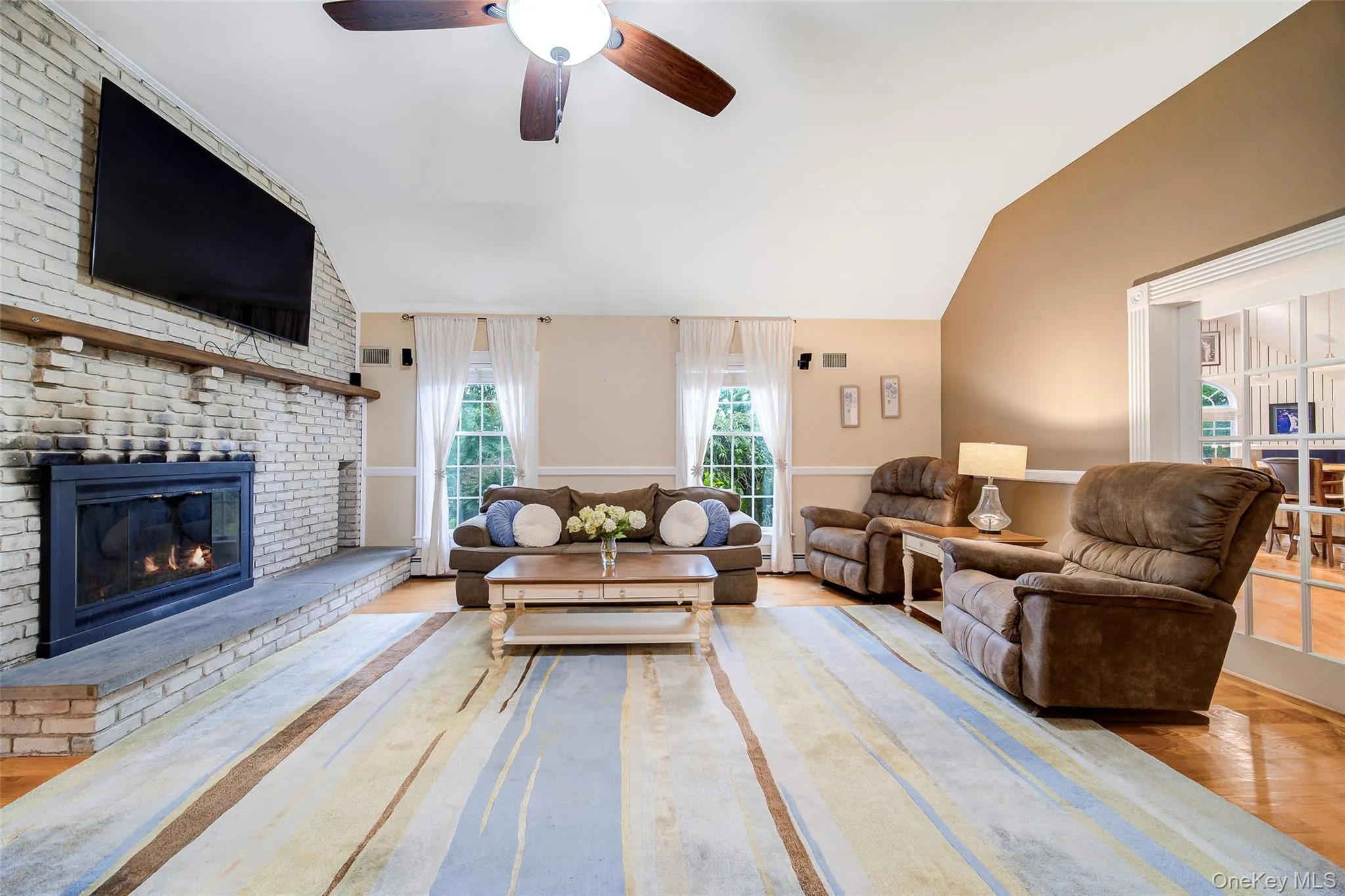 Vaulted ceiling, wood-finish flooring, white brick fireplace, ceiling fan, and French doors Vaulted ceiling, wood-finish flooring, white brick fireplace, ceiling fan, and French doors