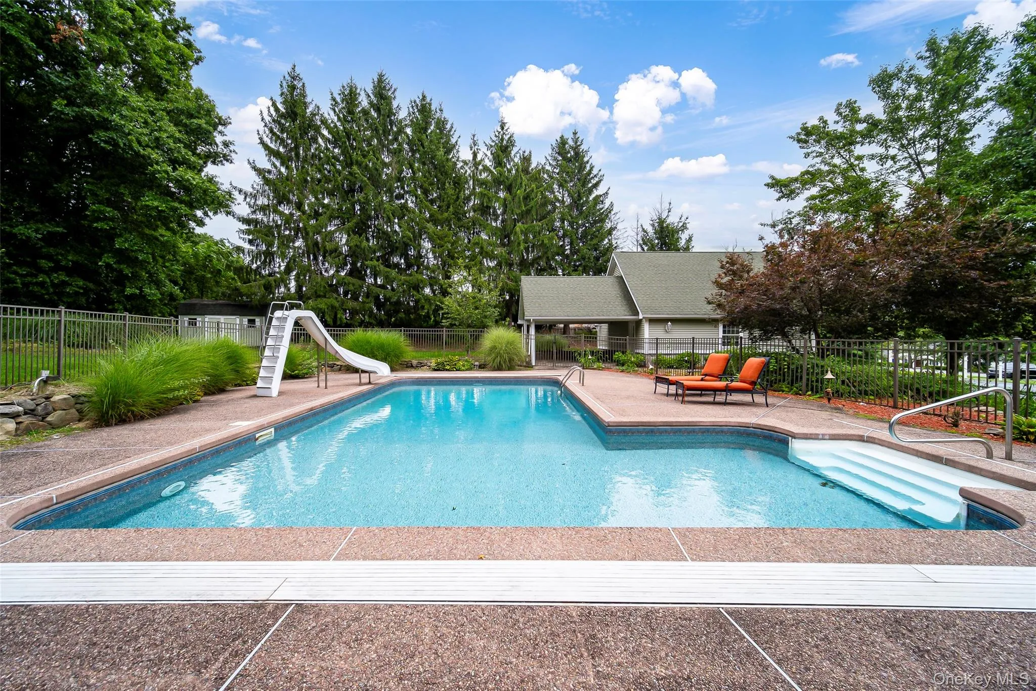In-ground swimming pool featuring a slide, broad entry steps, and surrounding concrete decking In-ground swimming pool featuring a slide, broad entry steps, and surrounding concrete decking