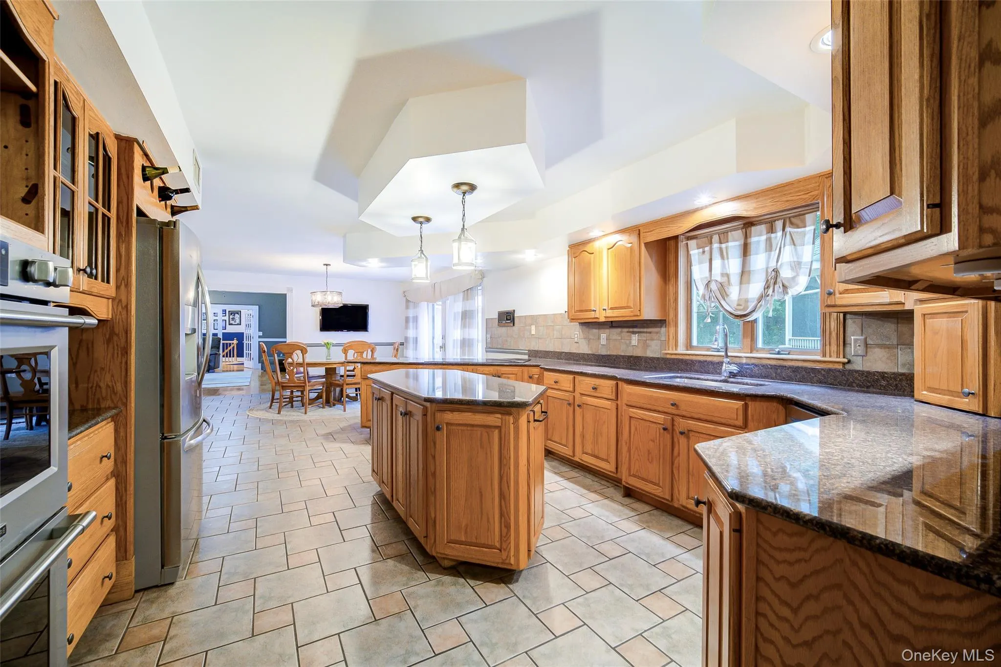 Expansive kitchen featuring wood cabinetry, granite countertops, a center island with ample storage, stainless steel appliances, and tile flooring Expansive kitchen featuring wood cabinetry, granite countertops, a center island with ample storage, stainless steel appliances, and tile flooring