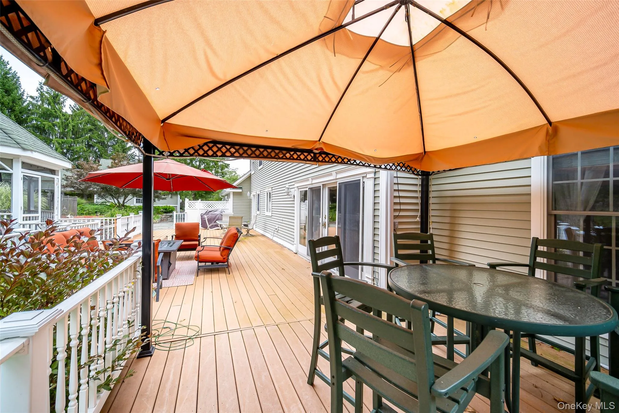 Expansive outdoor deck featuring a white baluster railing, and a covered dining area Expansive outdoor deck featuring a white baluster railing, and a covered dining area