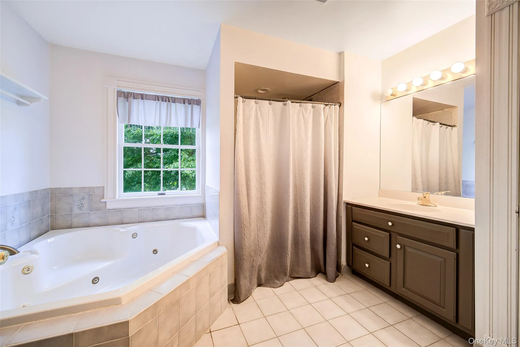 Corner soaking tub with tiled surround, single vanity, and tiled flooring Corner soaking tub with tiled surround, single vanity, and tiled flooring