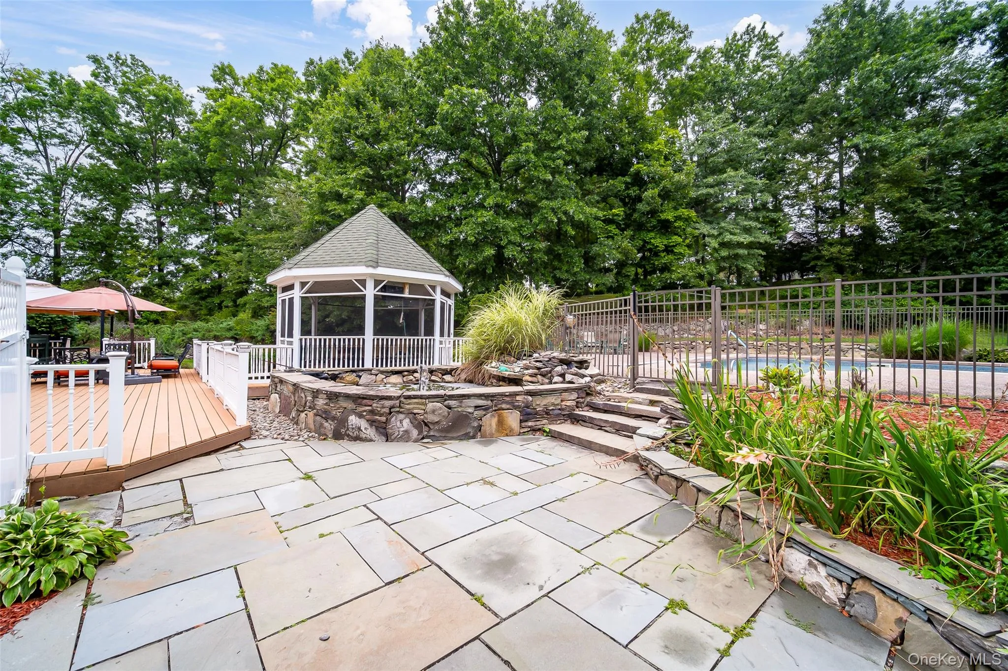 Stone patio with a screened gazebo, adjacent wood deck, and stone water feature Stone patio with a screened gazebo, adjacent wood deck, and stone water feature