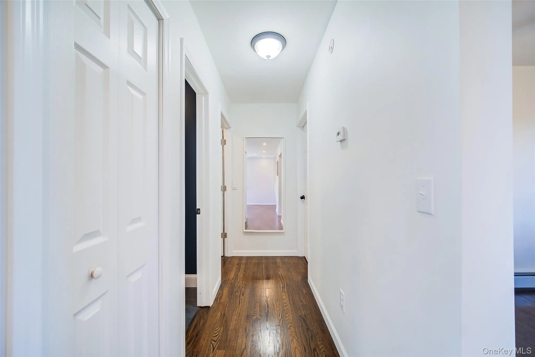 Hallway featuring wood-finish flooring, white walls, flush-mount lighting, and bi-fold doors Hallway featuring wood-finish flooring, white walls, flush-mount lighting, and bi-fold doors