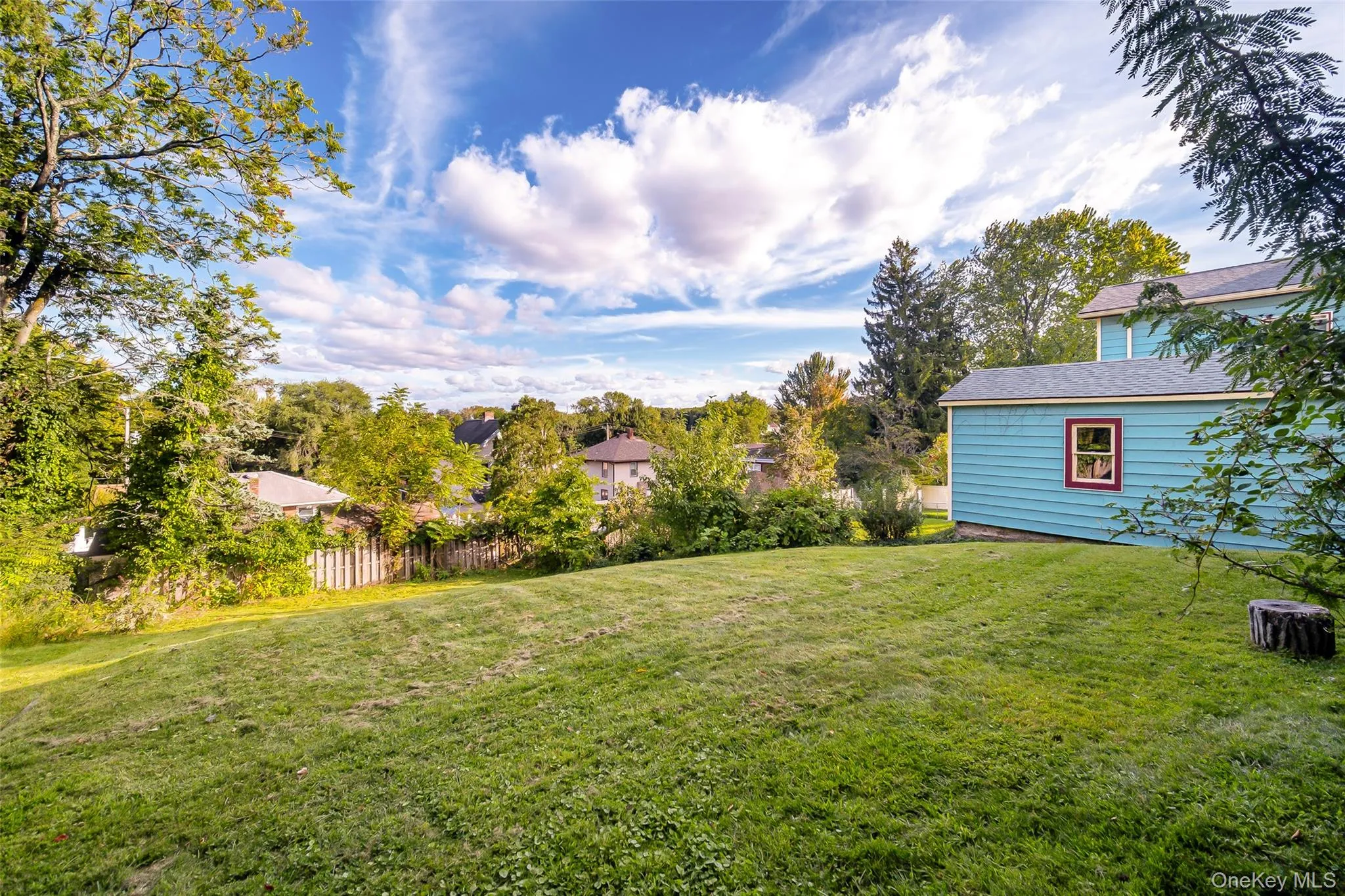 Expansive lawn with surrounding mature trees and a partial wood fence Expansive lawn with surrounding mature trees and a partial wood fence