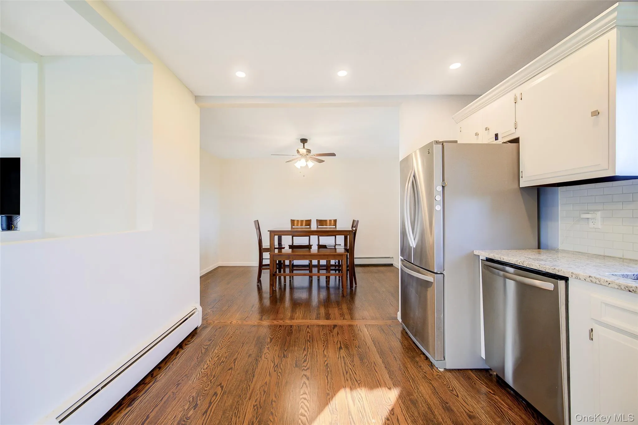 Wood-finish flooring throughout, recessed lighting, white cabinetry, stainless steel appliances, and a subway tile backsplash Wood-finish flooring throughout, recessed lighting, white cabinetry, stainless steel appliances, and a subway tile backsplash