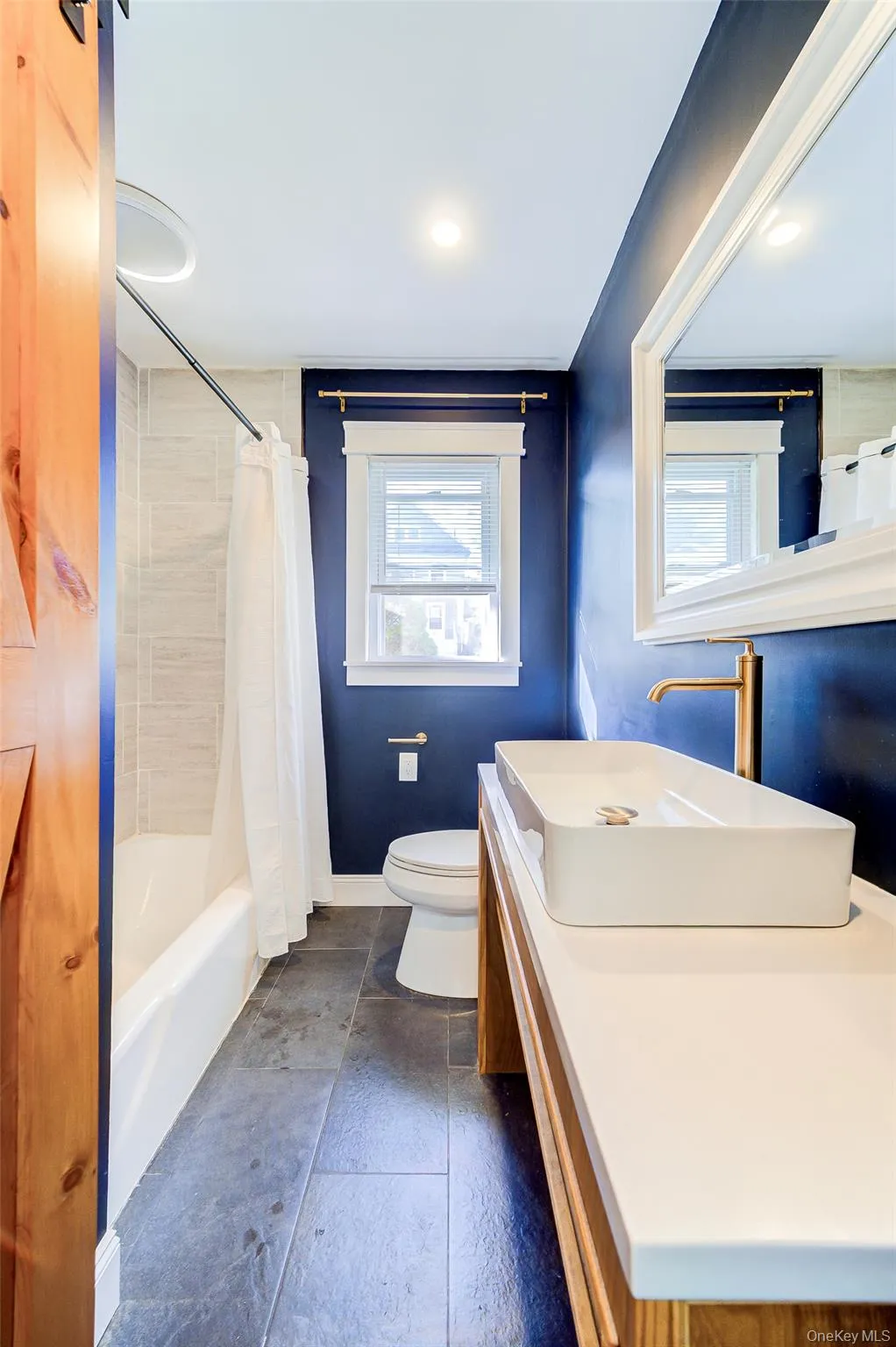 Bathroom featuring a custom made modern vanity with an elongated vessel sink, stone white countertop, and gold-finish fixtures Bathroom featuring a custom made modern vanity with an elongated vessel sink, stone white countertop, and gold-finish fixtures