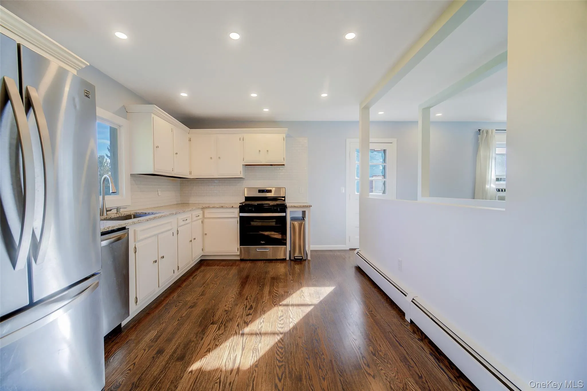 Kitchen featuring stainless steel appliances, white cabinetry, wood-finish flooring, recessed lighting, and a subway tile backsplash Kitchen featuring stainless steel appliances, white cabinetry, wood-finish flooring, recessed lighting, and a subway tile backsplash