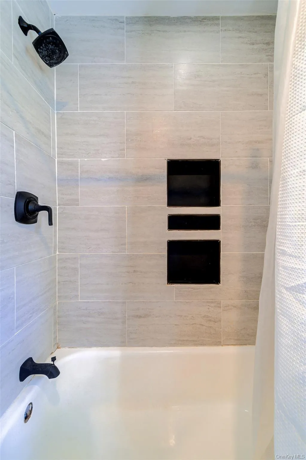 Shower/Bathtub has light gray tile surround, matte black shower fixtures, and built-in shower niches. Shower/Bathtub has light gray tile surround, matte black shower fixtures, and built-in shower niches.