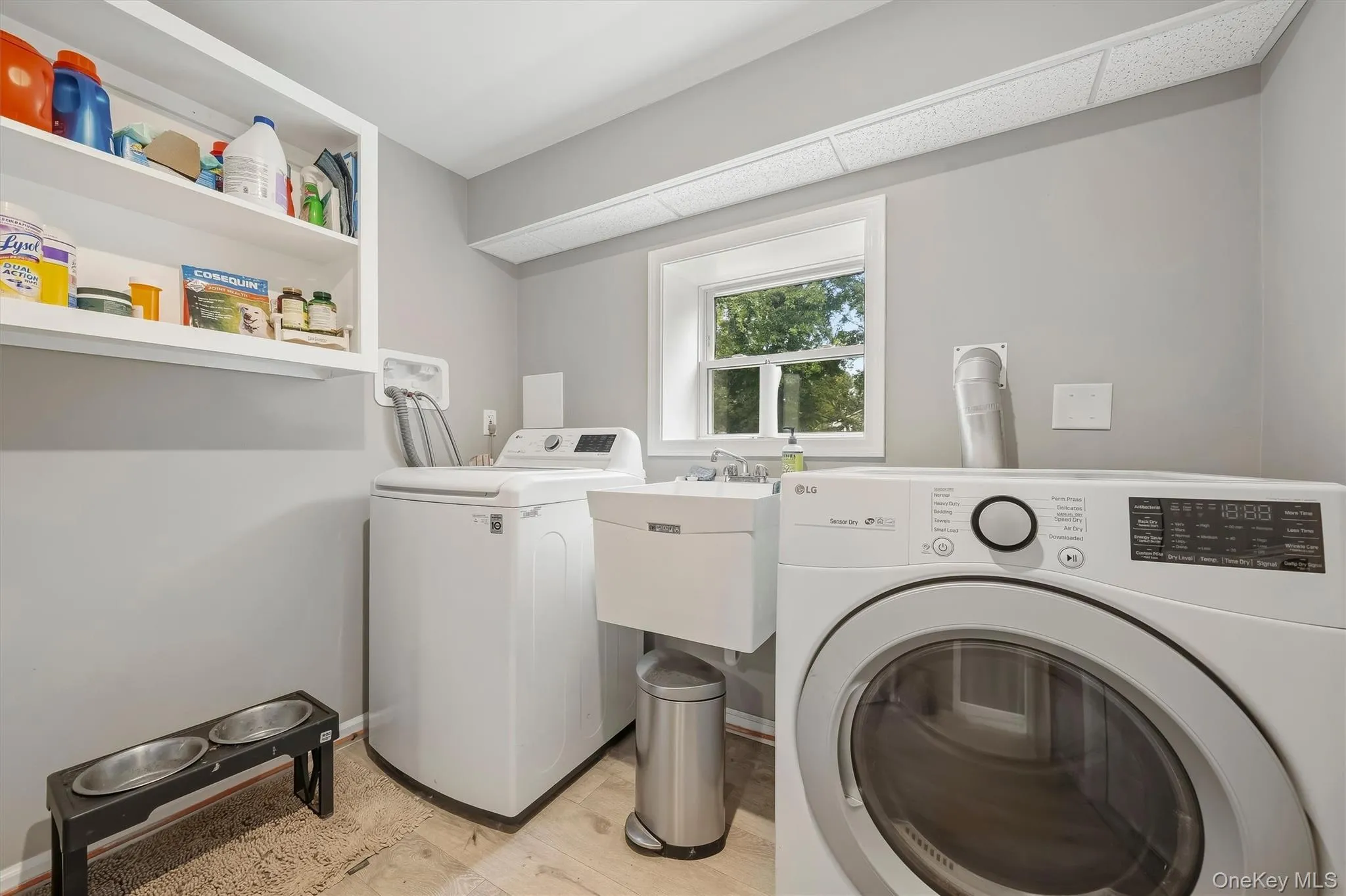 Laundry area featuring a utility sink, open shelving, and a window Laundry area featuring a utility sink, open shelving, and a window