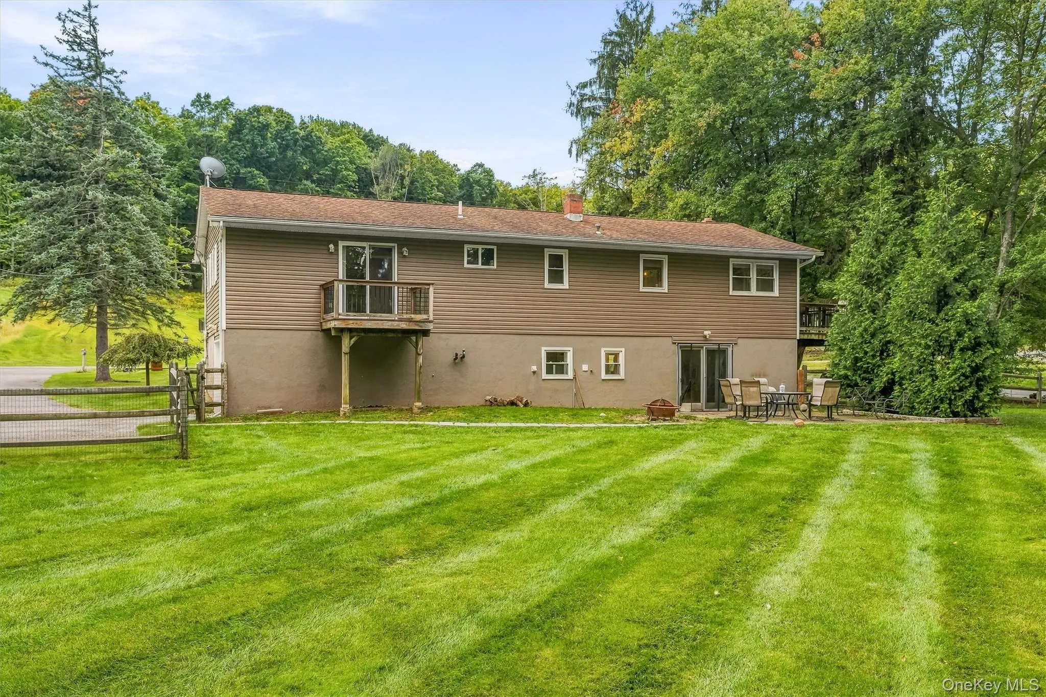 Expansive green space featuring a wood fence, mature trees, and a ground-level patio Expansive green space featuring a wood fence, mature trees, and a ground-level patio
