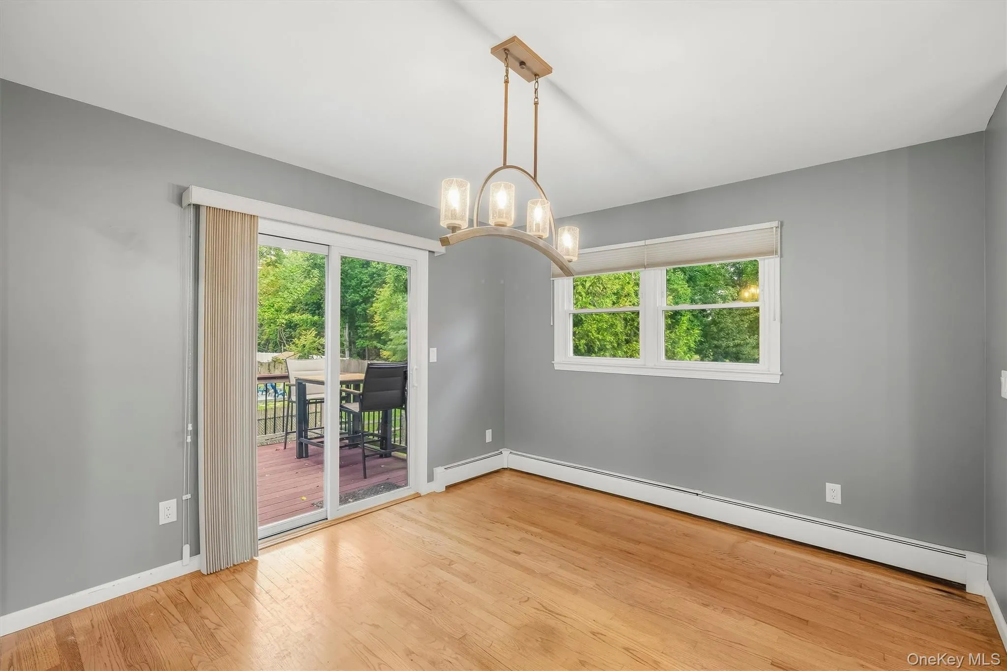 Hardwood flooring, sliding glass door with exterior deck, multiple windows, and a ceiling-mounted light fixture Hardwood flooring, sliding glass door with exterior deck, multiple windows, and a ceiling-mounted light fixture