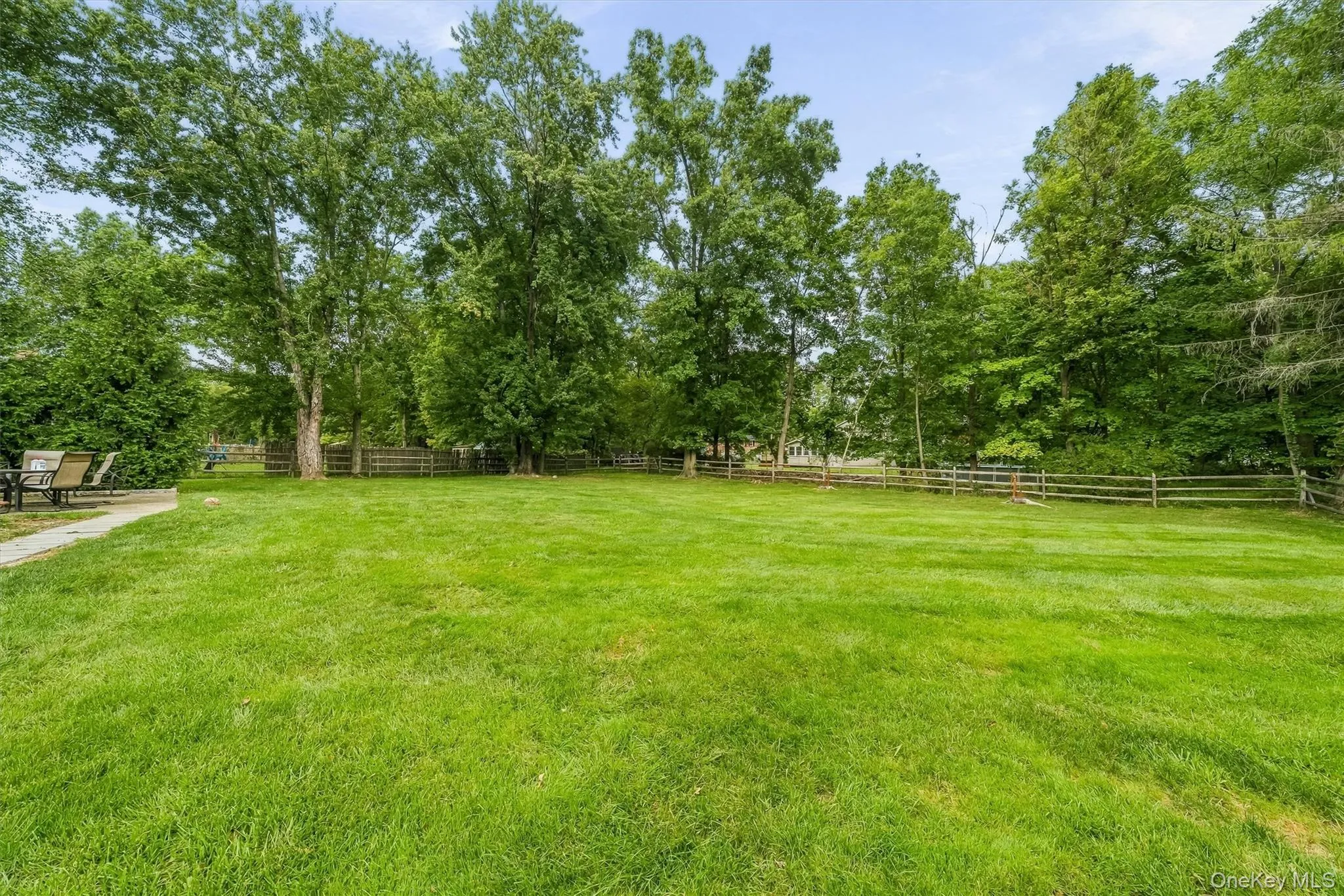 Expansive green lawn framed by mature trees and a rustic wooden fence Expansive green lawn framed by mature trees and a rustic wooden fence