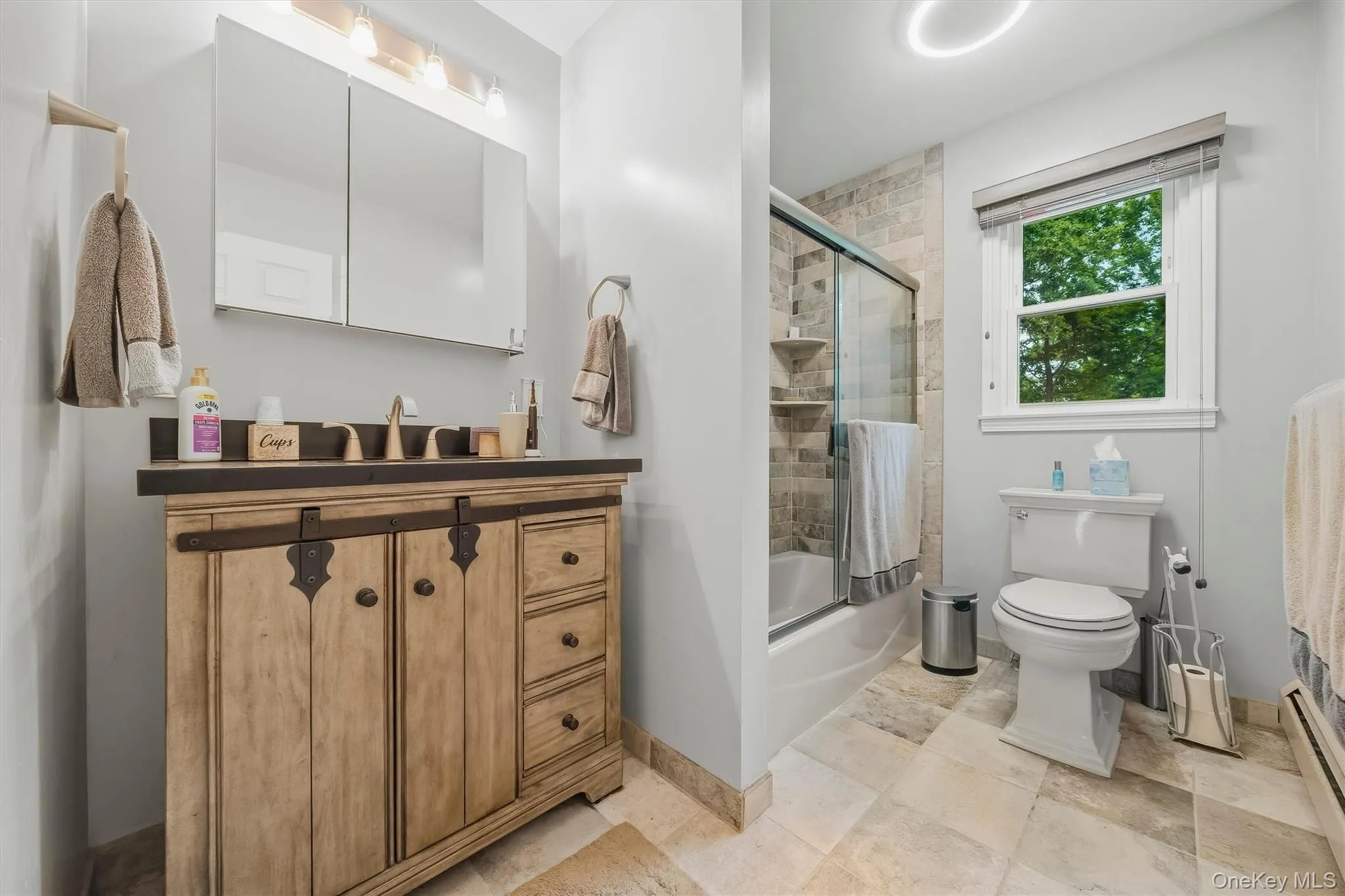 Wood-finish vanity with dark countertop, dual mirrored medicine cabinet, and a glass-enclosed shower with tiled surround Wood-finish vanity with dark countertop, dual mirrored medicine cabinet, and a glass-enclosed shower with tiled surround