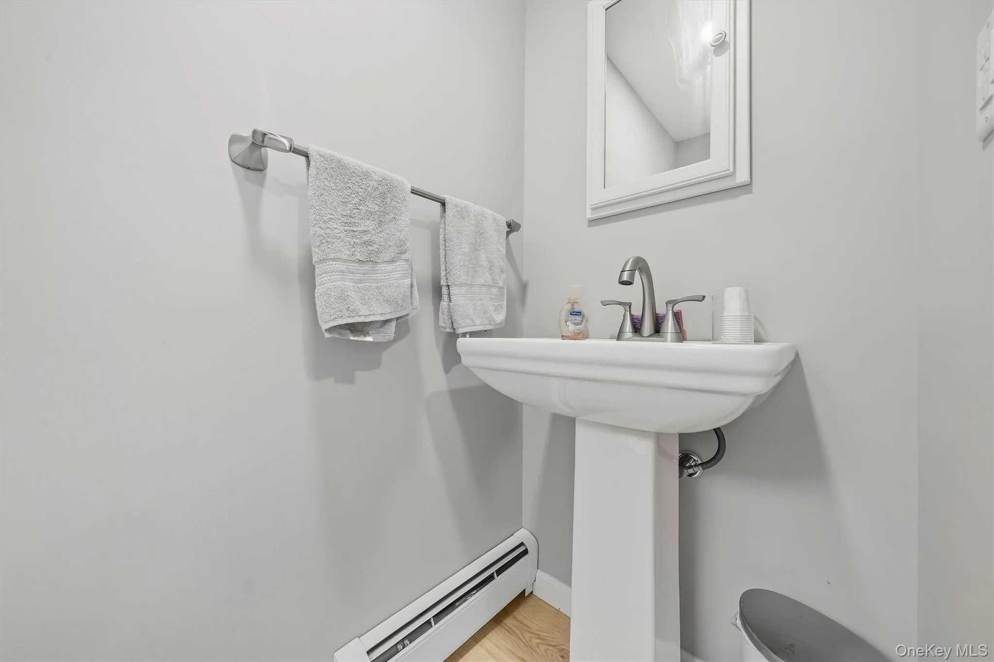 Pedestal sink with a polished chrome faucet, mirrored medicine cabinet, and light-toned wood-finish flooring Pedestal sink with a polished chrome faucet, mirrored medicine cabinet, and light-toned wood-finish flooring